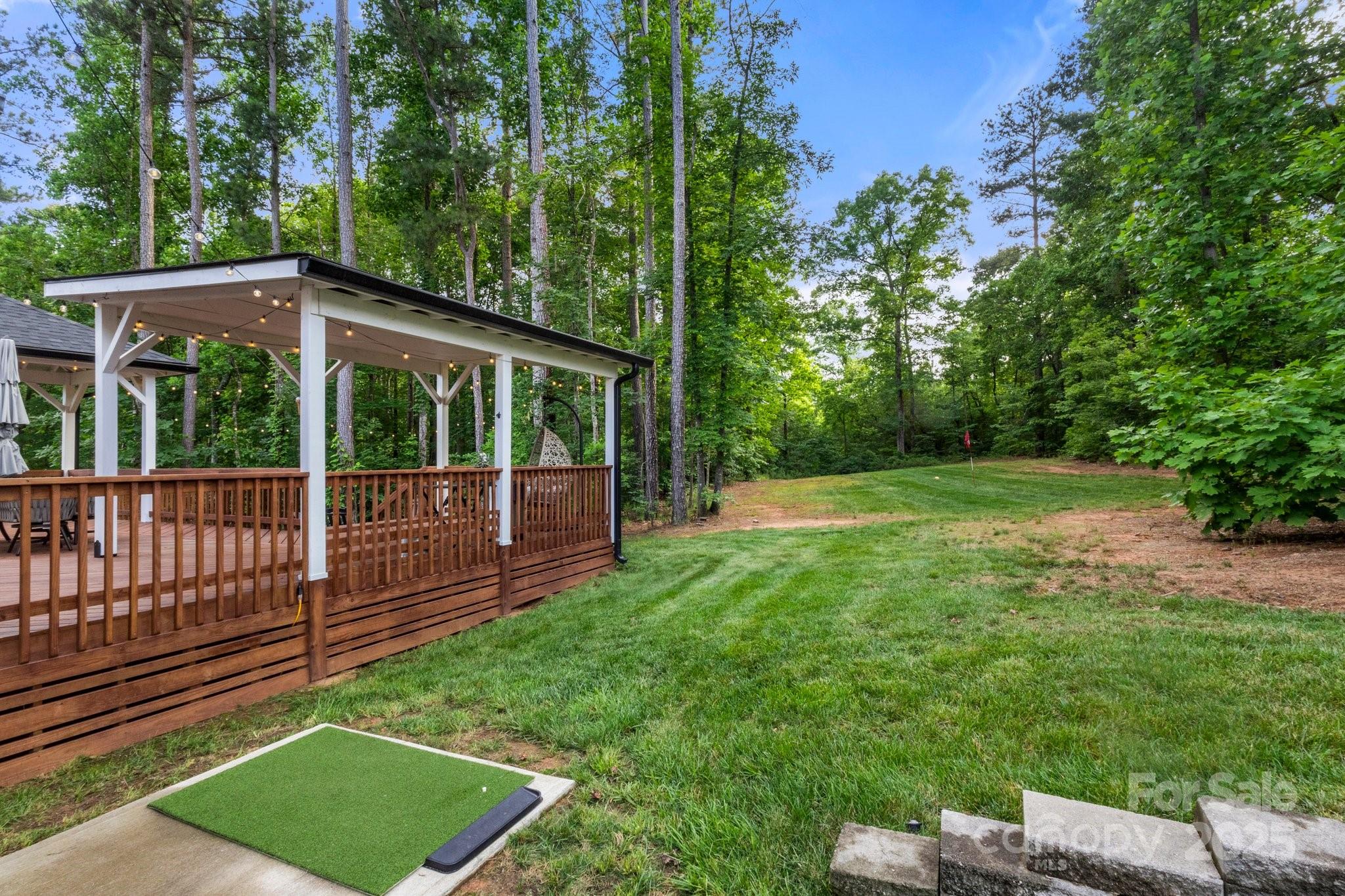 Wooded backyard with a covered deck, string lights, and a small putting green.