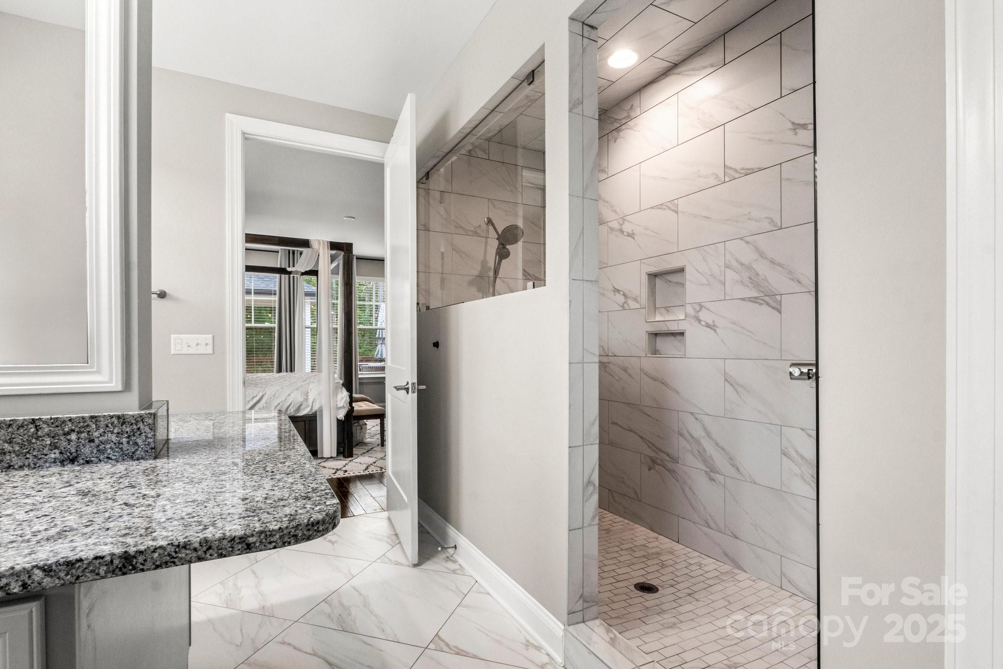 Marble-look tiled walk-in shower with recessed niches beside a granite vanity.