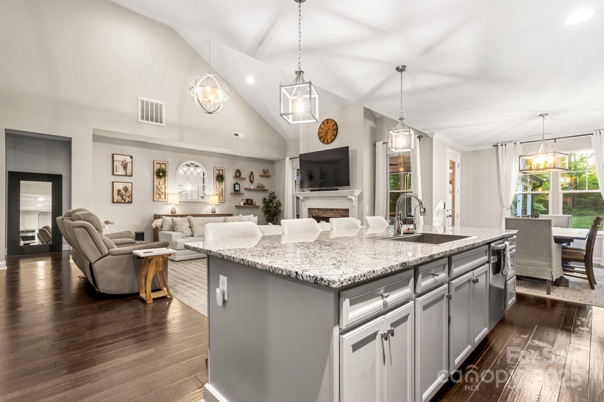 Open-plan kitchen and living room with a granite island, vaulted ceiling, and fireplace.