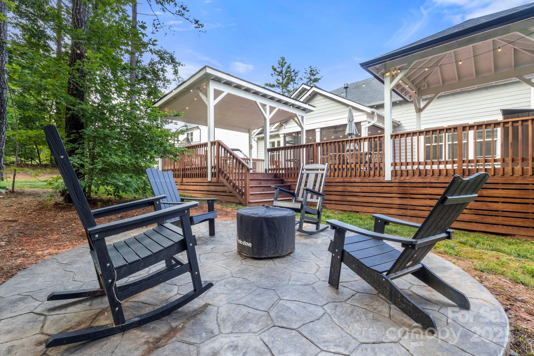 Stone patio with Adirondack chairs and fire pit beside a covered wooden deck.