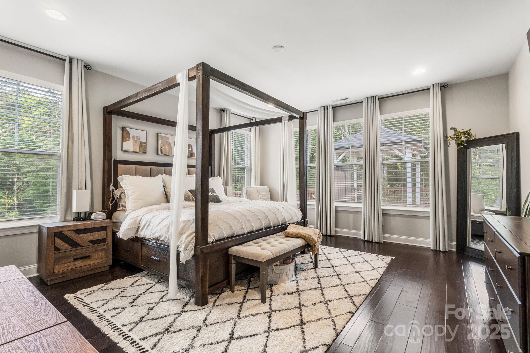 Furnished bedroom with a dark wood canopy bed, white bedding, and large curtained windows.
