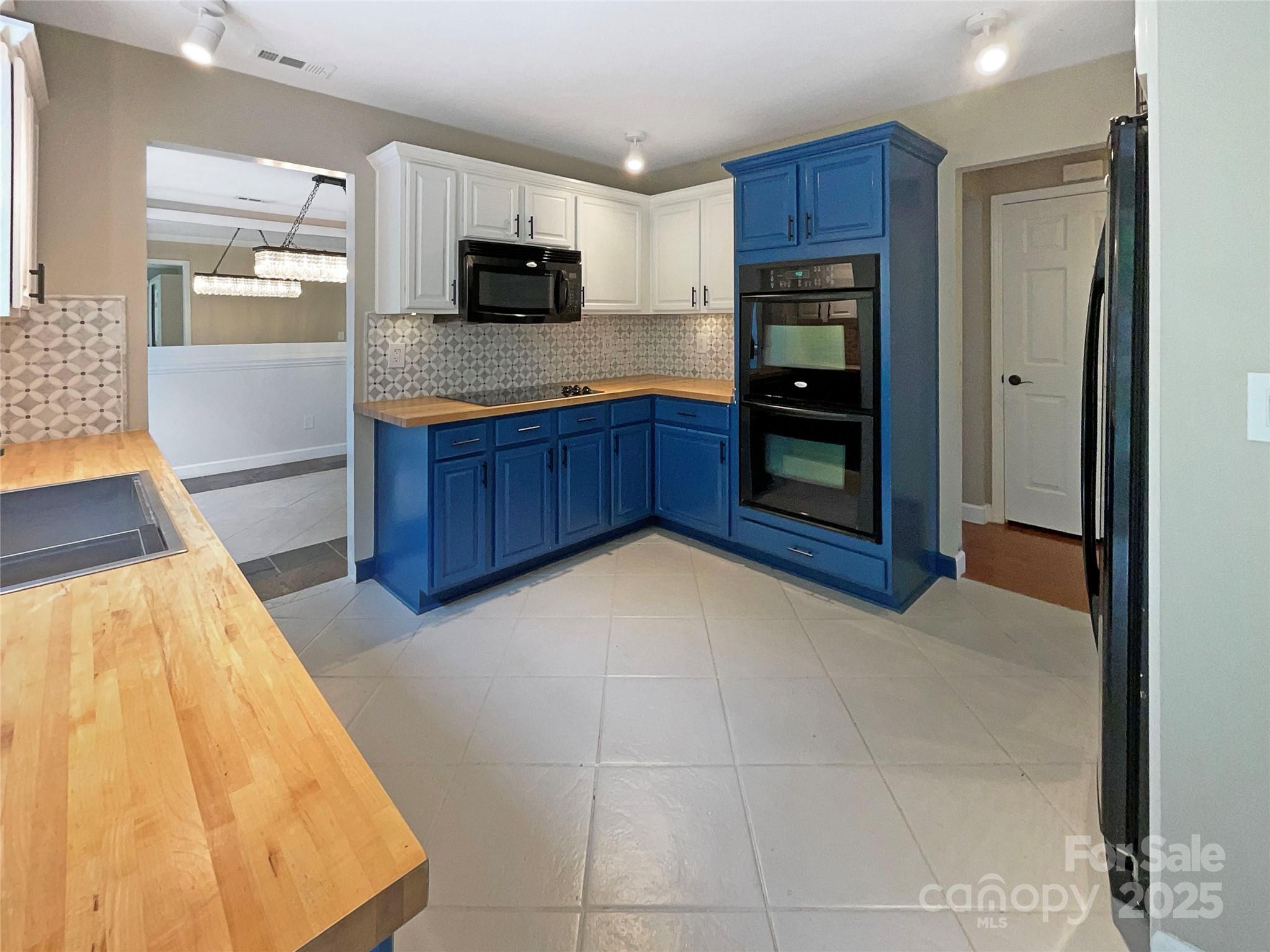 Kitchen with blue cabinetry, a double oven, patterned backsplash, and butcher-block counters.