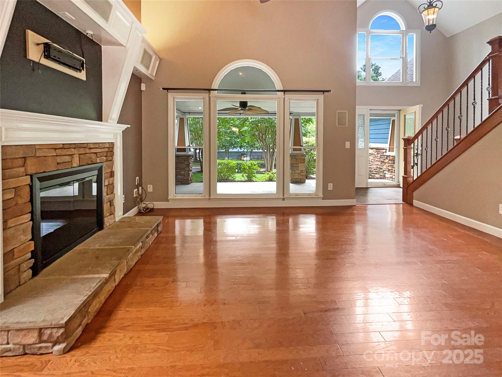 Vacant living room with a raised stone fireplace, polished hardwood floors, and tall arched windows.