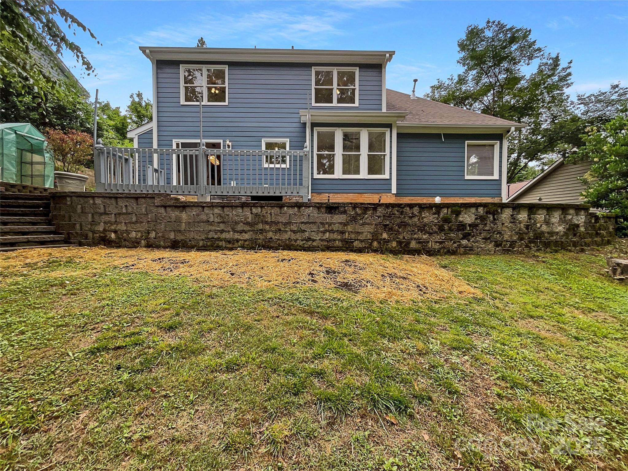 Blue two-story home with a raised deck, stone retaining wall, and grassy backyard.