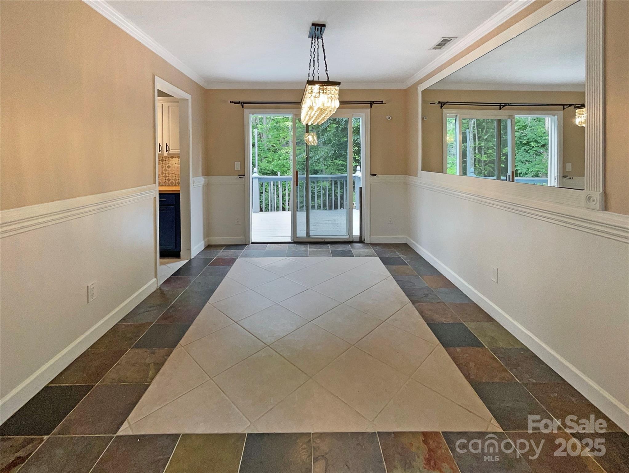 Unfurnished dining room with a crystal chandelier, patterned tile floor, and sliding doors to a wooded deck.