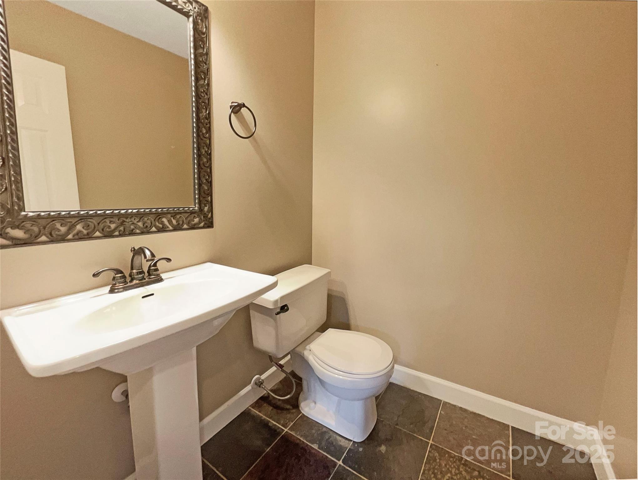 Bathroom with a white pedestal sink, toilet, ornate mirror, and dark tile floor.