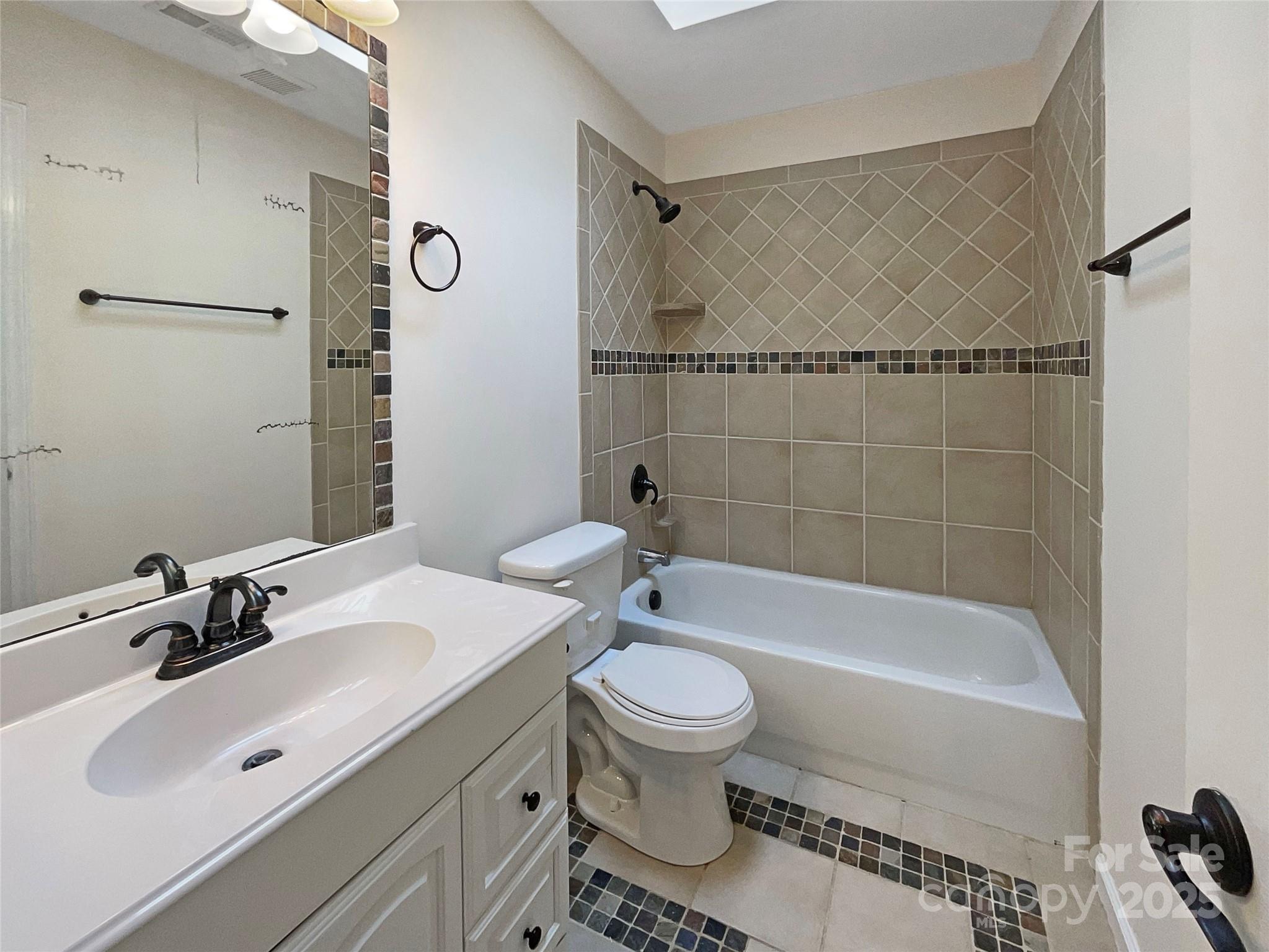 Bathroom with a white vanity, toilet, and bathtub framed by beige diamond-pattern tile.