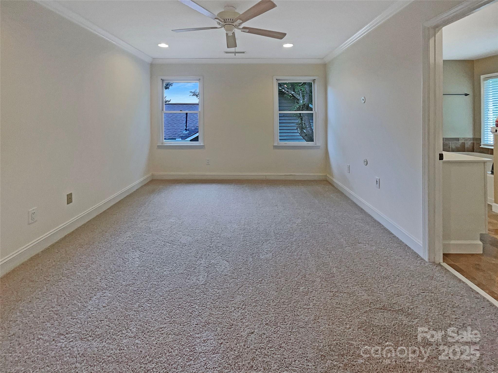 Empty carpeted bedroom with two windows, a ceiling fan, and a bathroom doorway.