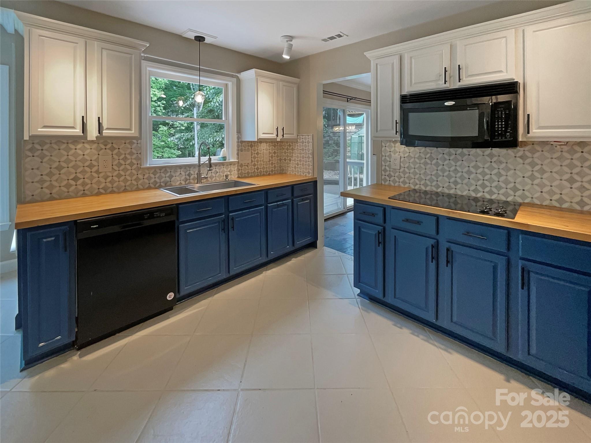 Kitchen with navy lower cabinets, butcher-block counters, patterned tile backsplash, and a sink beneath a window.
