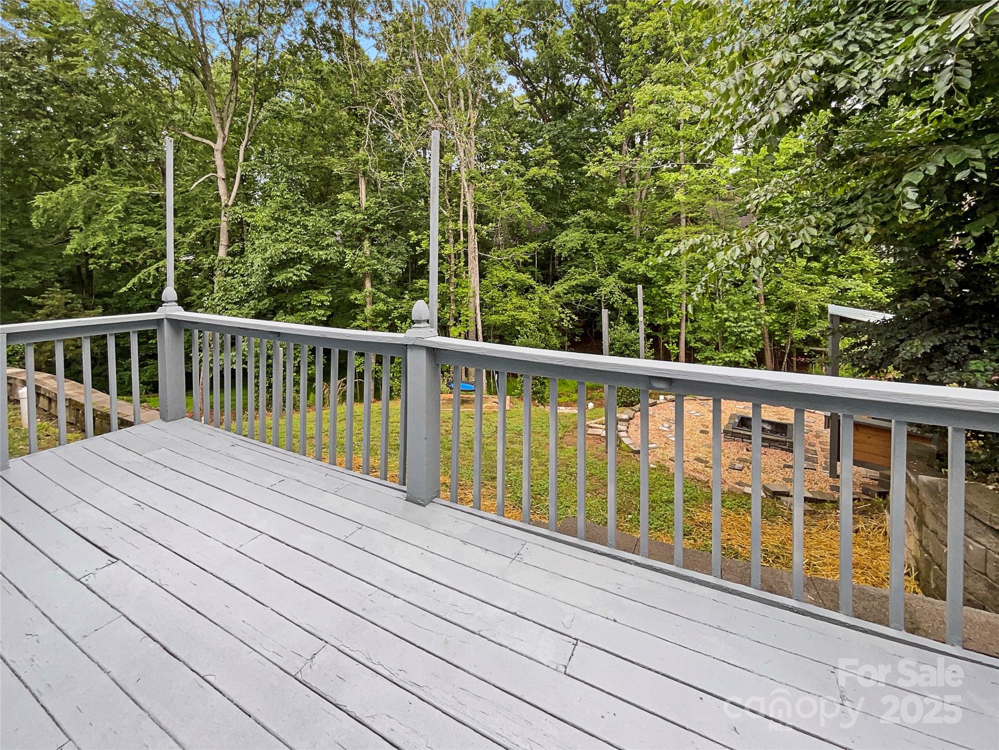 Gray wooden deck overlooking a wooded backyard and stone patio.