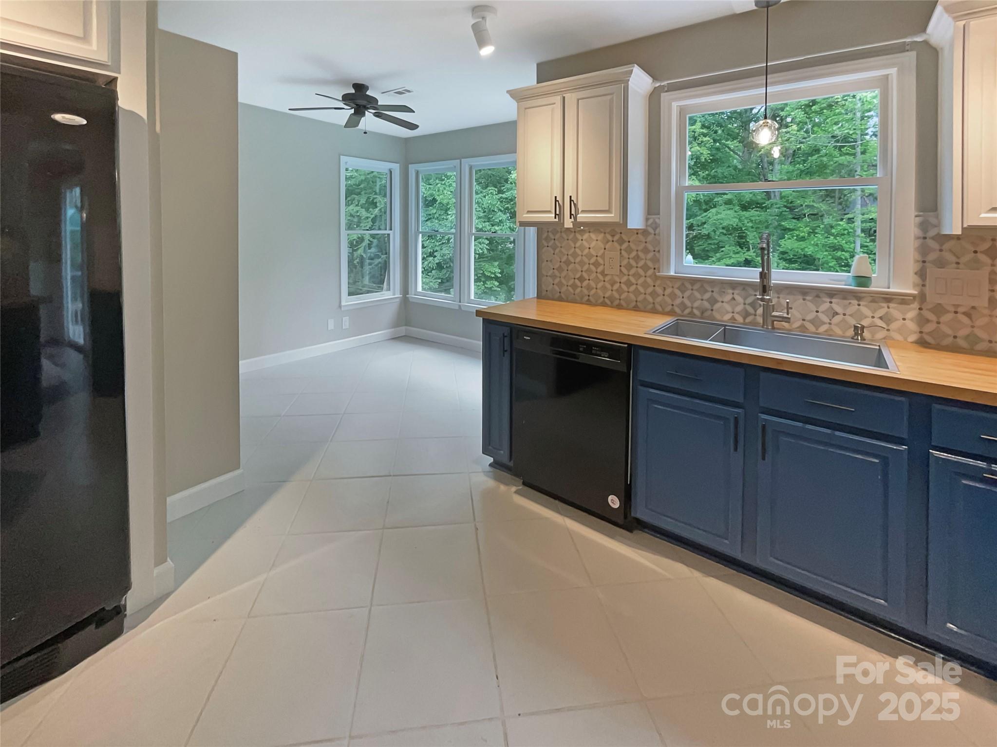 Kitchen with navy cabinets, wood counters, patterned backsplash, and windows overlooking trees.