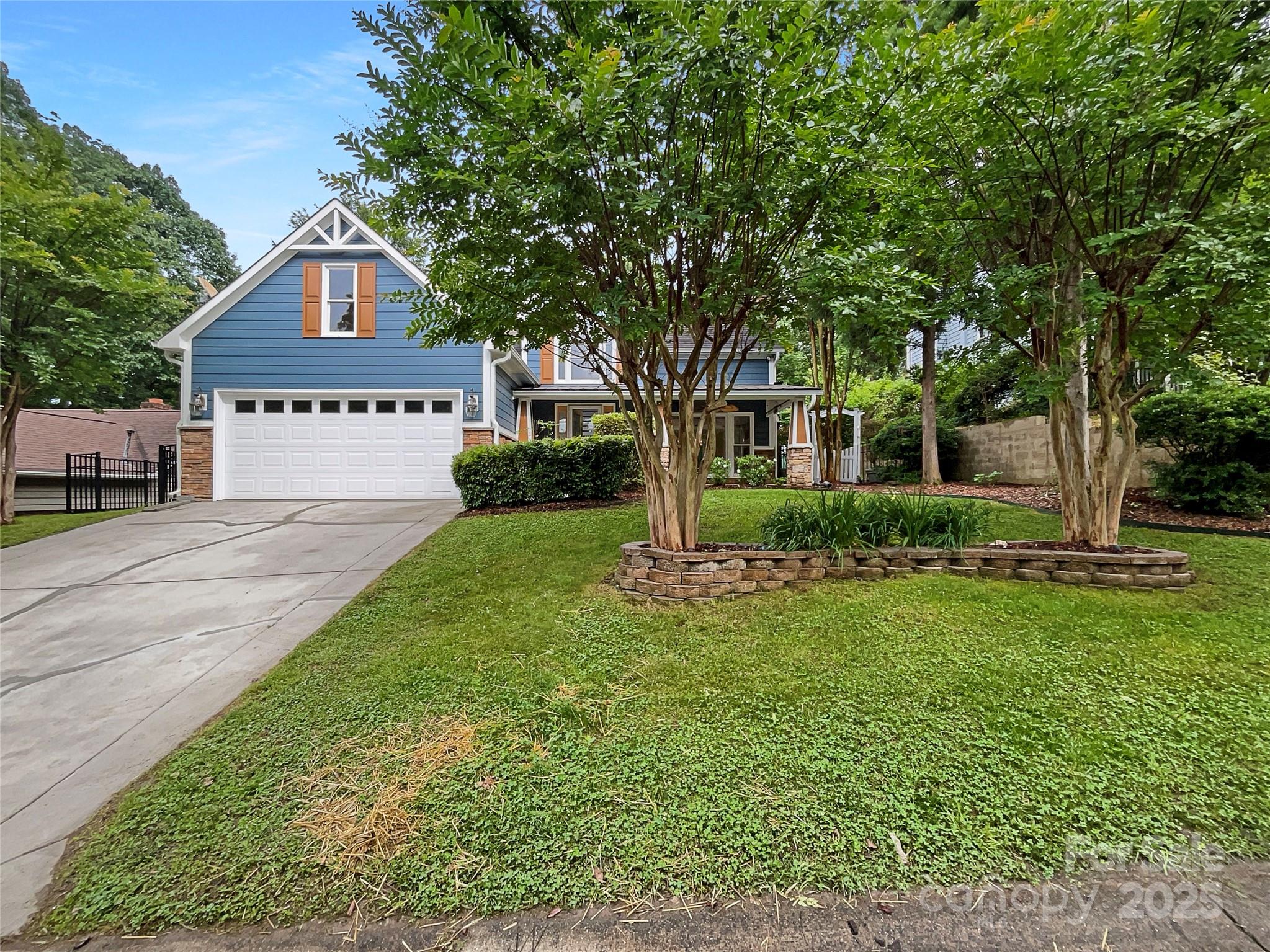 Blue two-story home with orange shutters, a white double garage, and a tree-shaded front lawn.