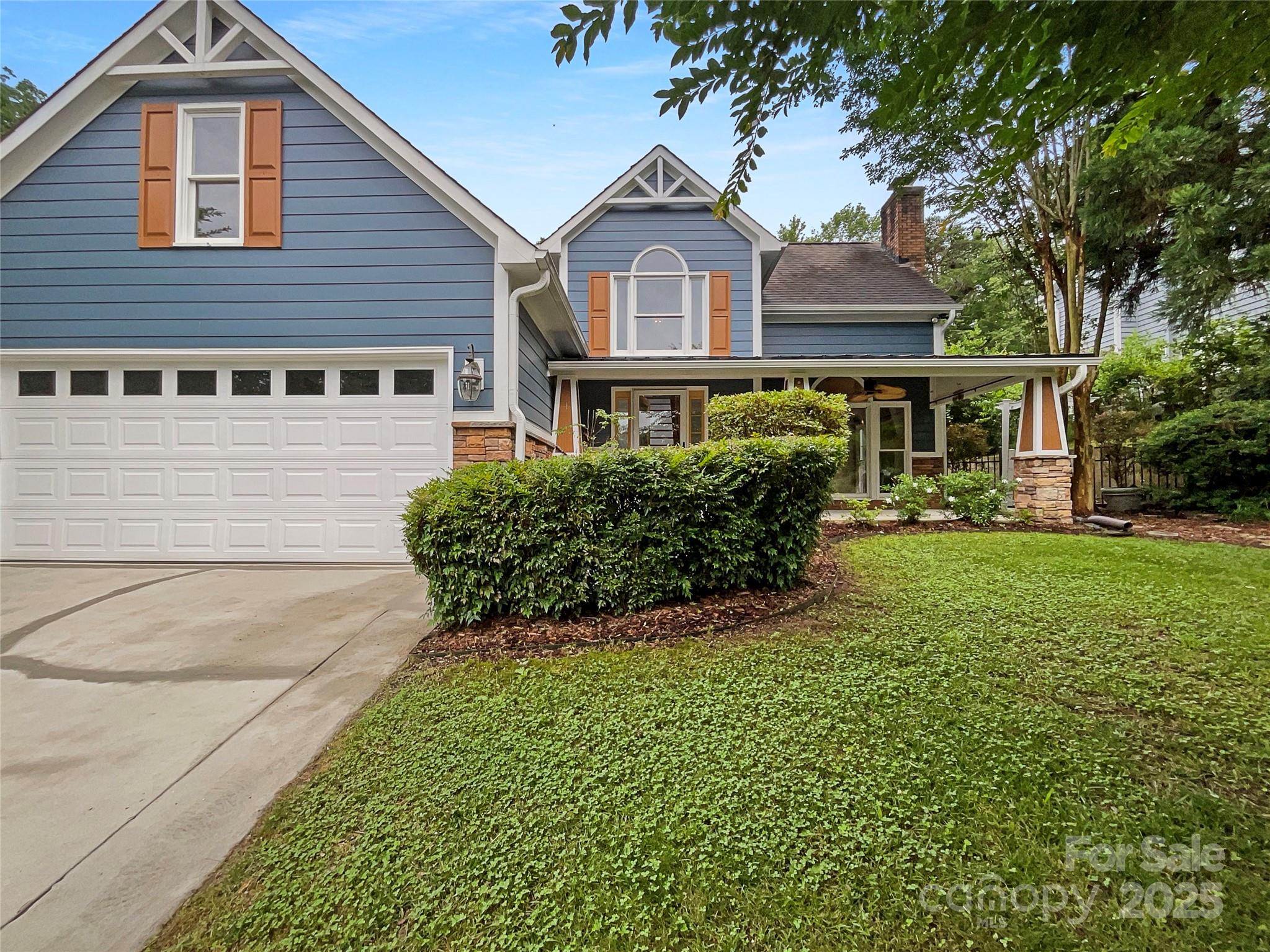Blue two-story house with orange shutters, a double garage, covered porch, and landscaped lawn.