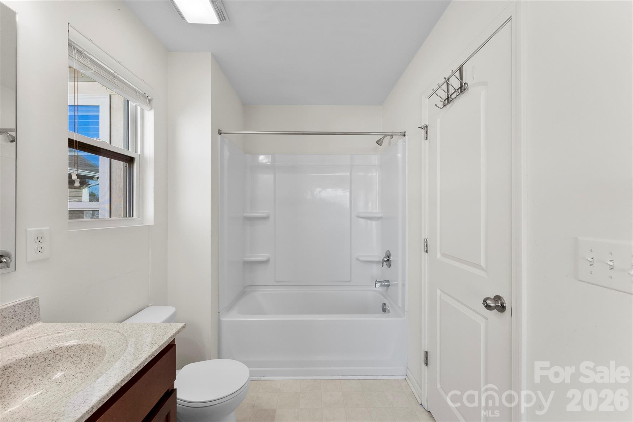 Bathroom with a white tub and shower, granite countertop, and window with blinds.