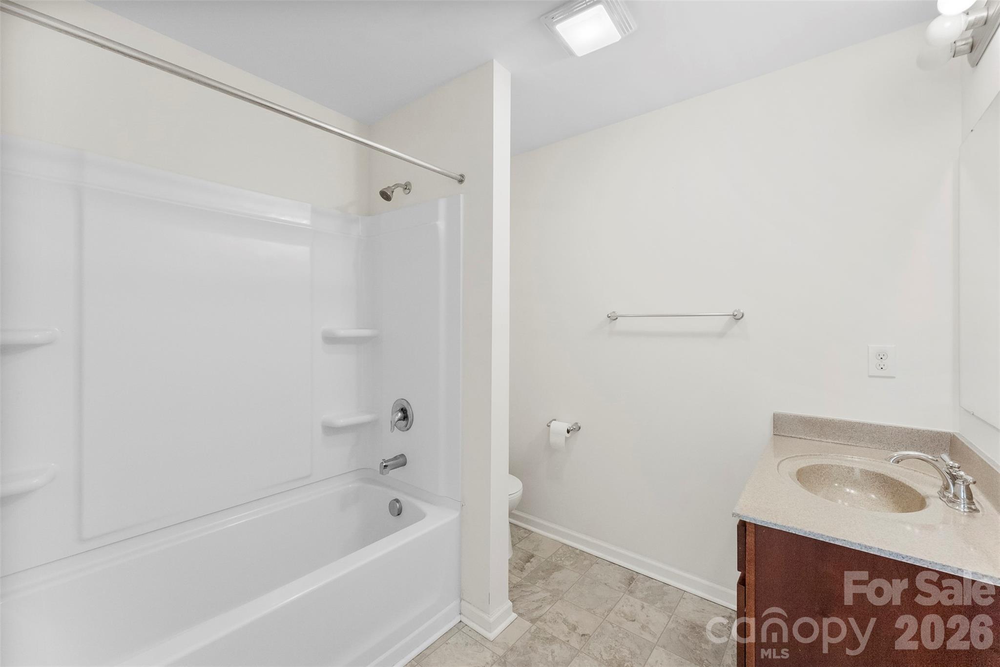 Bathroom with a white tub and shower, tiled floor, and wood vanity with oval sink.