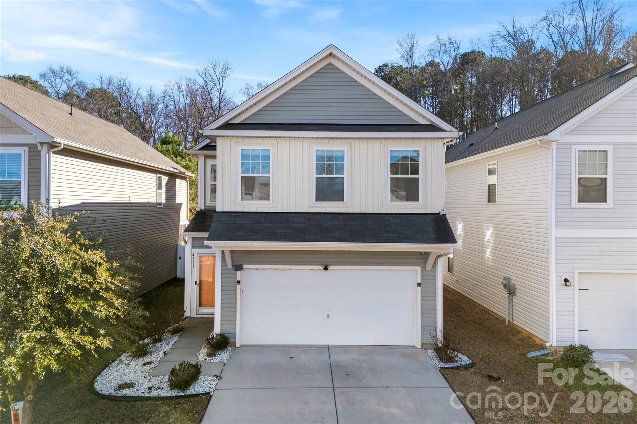 Two-story gray-and-white house with a front gable, two-car garage, and landscaped walkway.