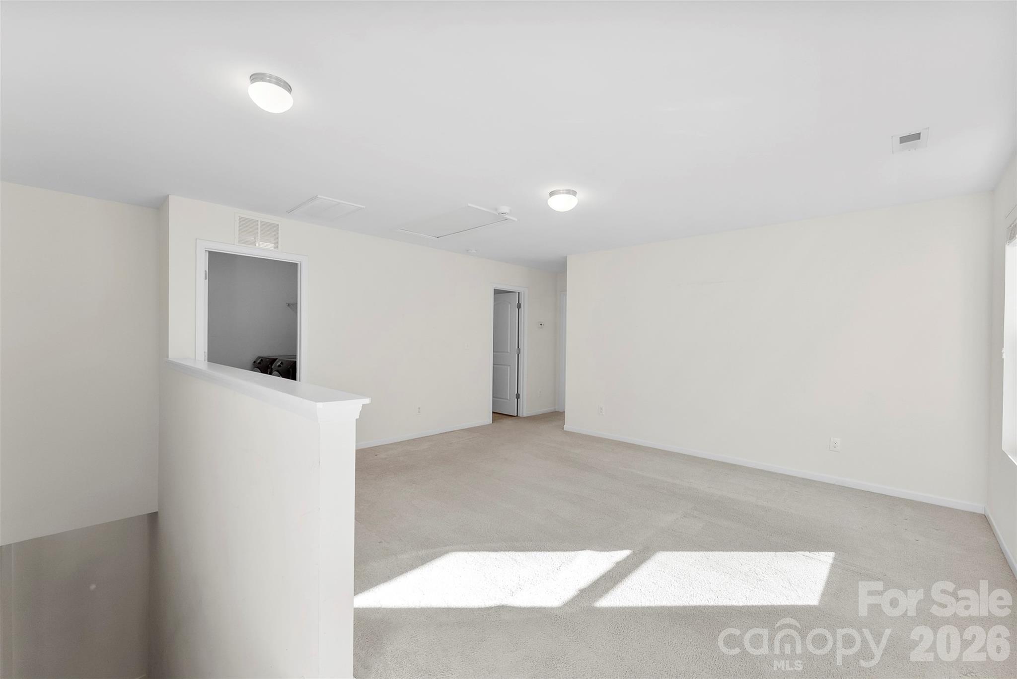 Empty carpeted living room with a pass-through opening and bright sunlight across the floor.