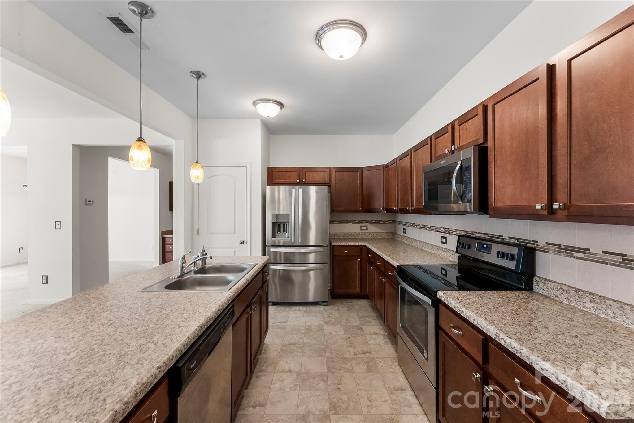 Kitchen with dark wood cabinets, granite countertops, a large sink island, and stainless steel appliances.