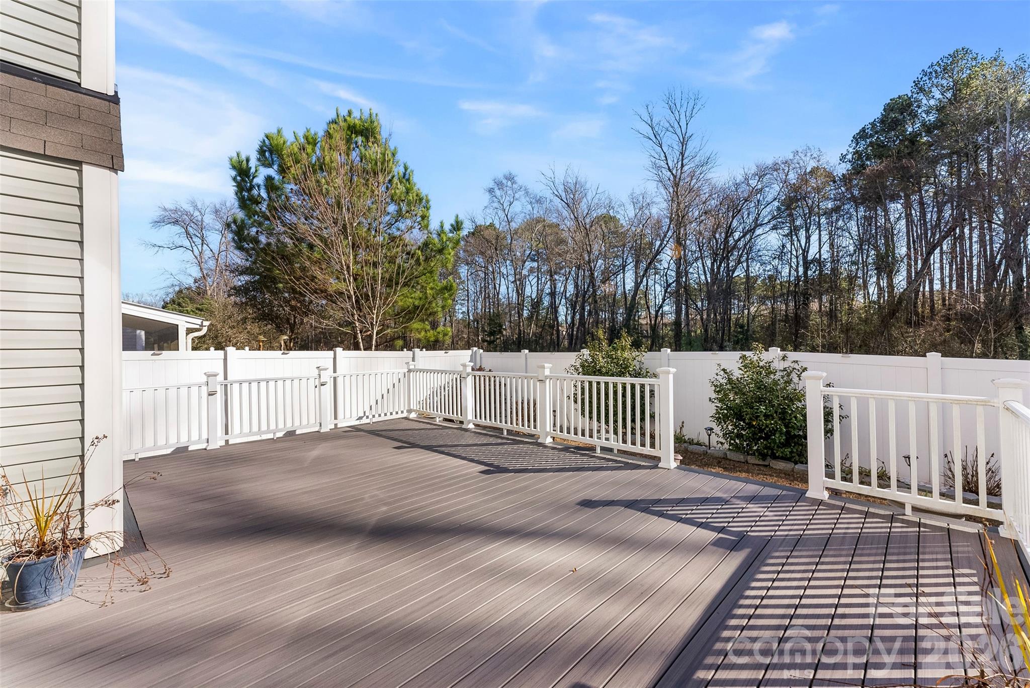 Spacious gray backyard deck with white railings and a fenced, wooded yard beyond.