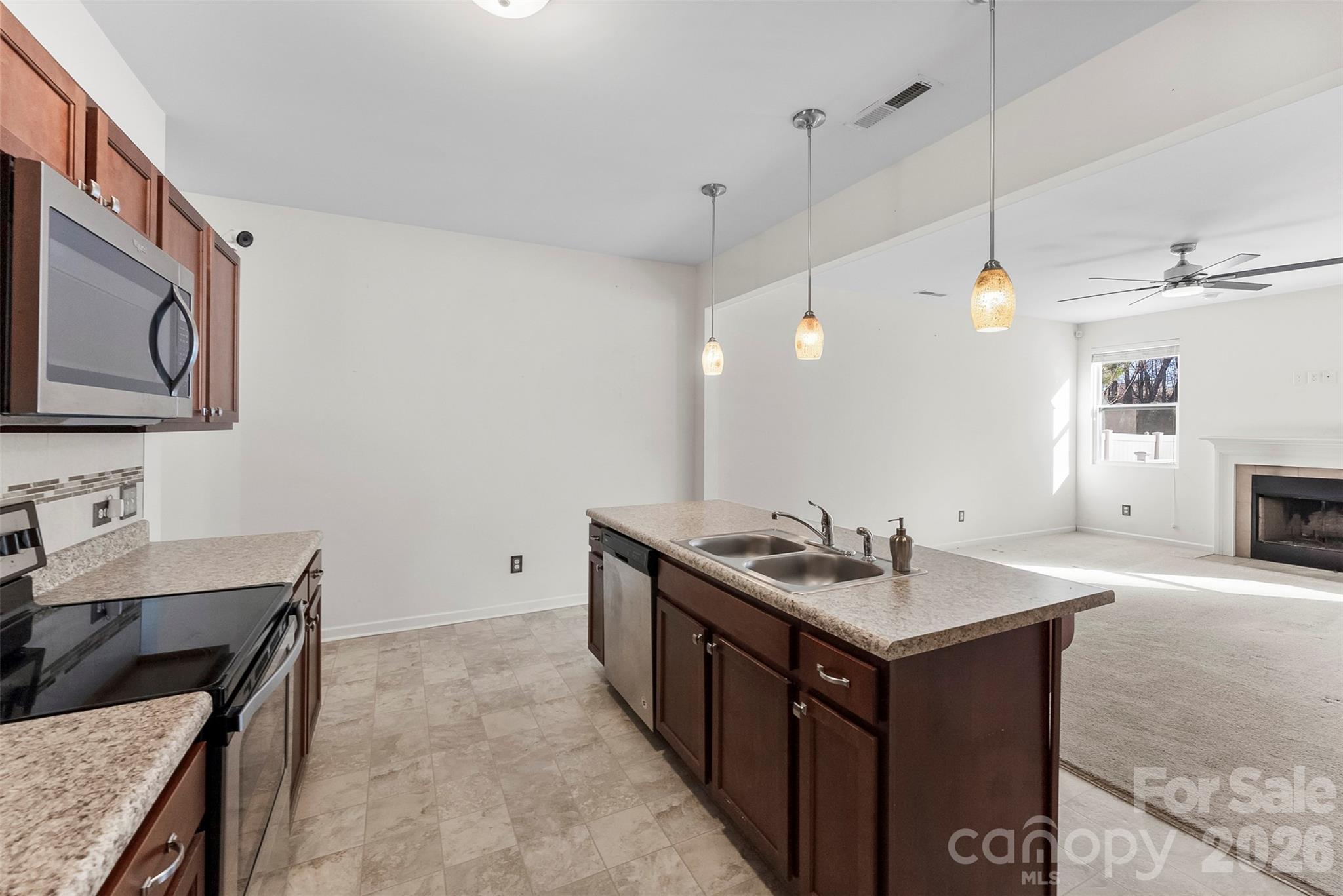 Kitchen with a large granite island and pendant lights opening to a living room with a fireplace.