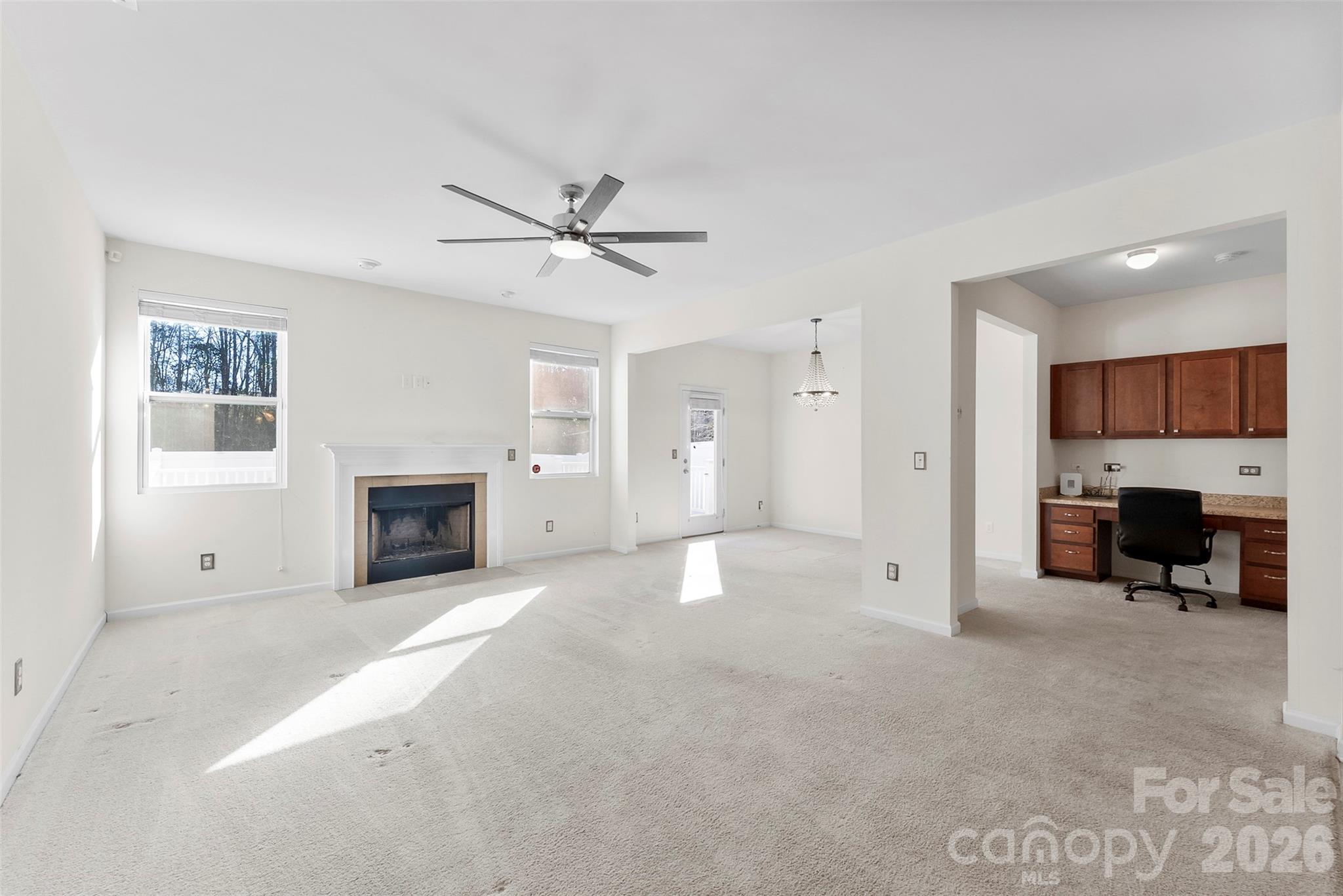 Vacant living room with a fireplace, ceiling fan, and adjoining built-in desk nook.