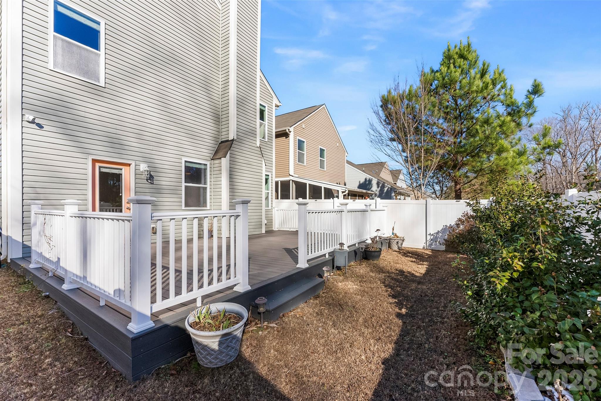 Raised backyard deck with white railings beside a gray-sided house and white privacy fence.