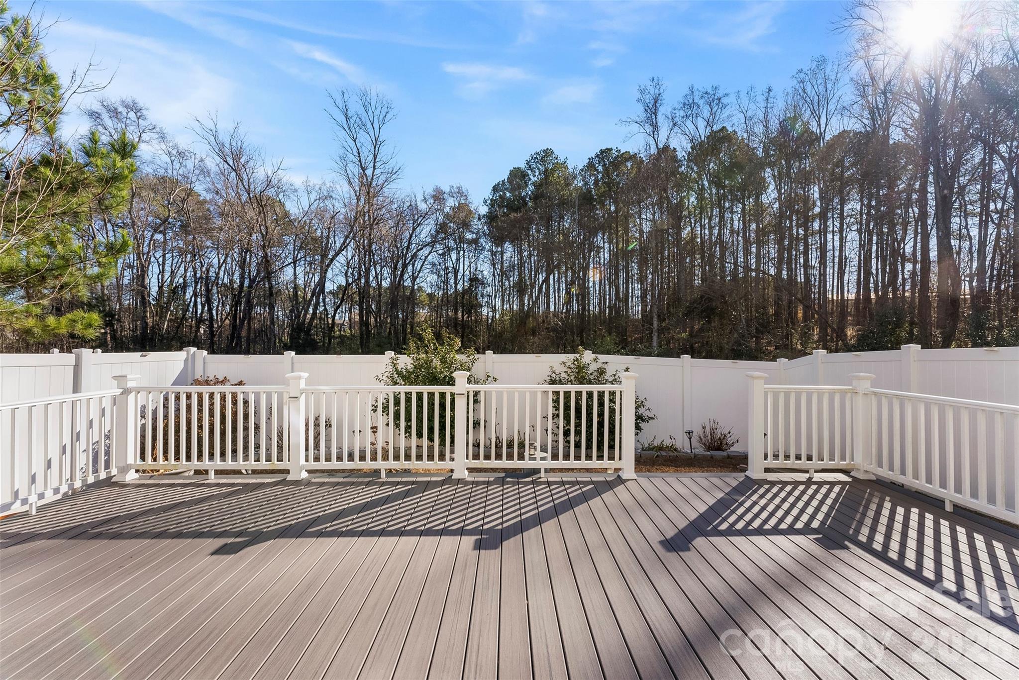 Spacious gray deck with white railings and a privacy fence overlooking leafless trees.