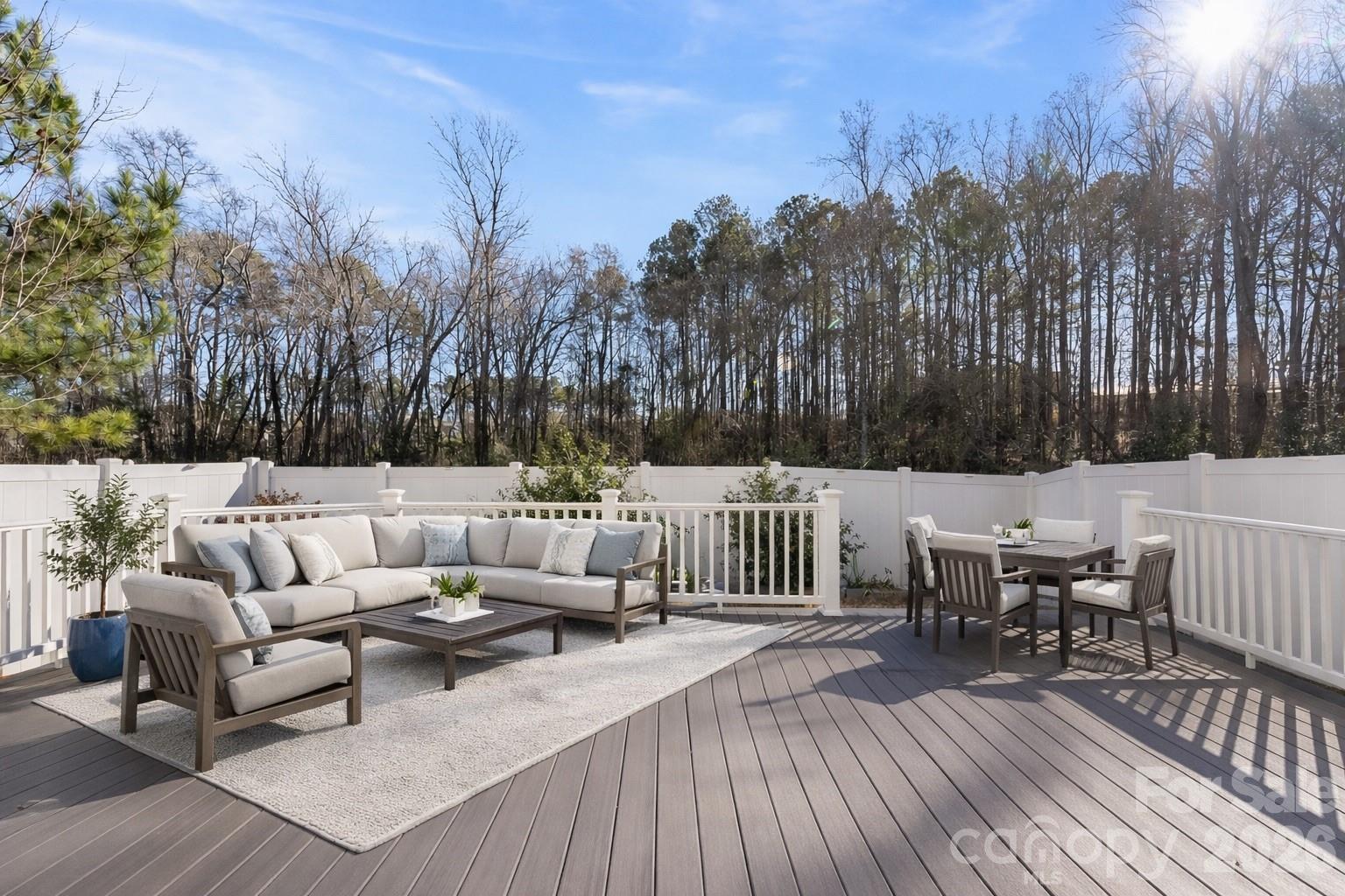 Outdoor deck with sectional seating, dining set, white railings, and a wooded backdrop.