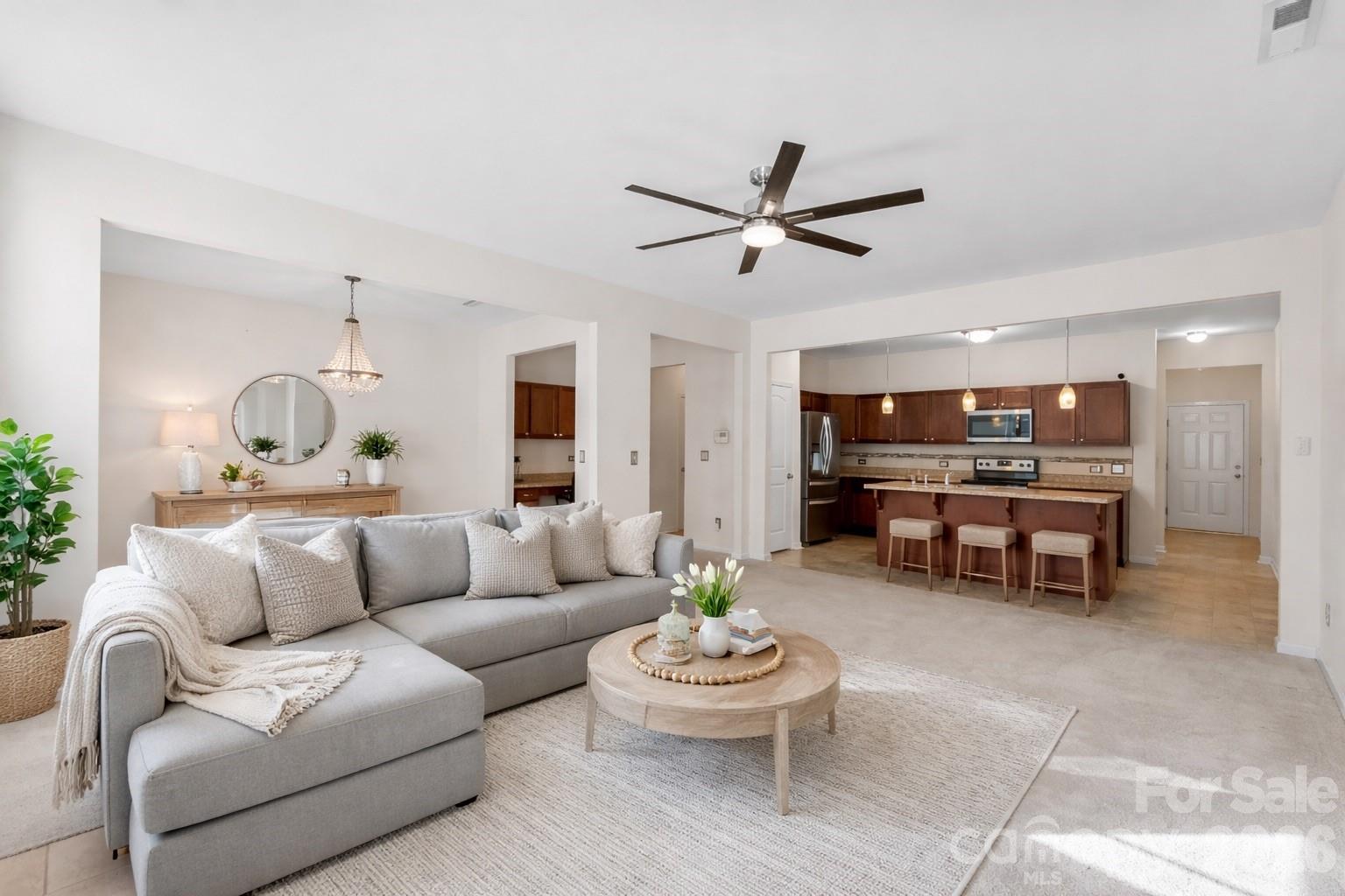 Open-plan living room with a gray sectional and round coffee table beside a kitchen with a breakfast bar.