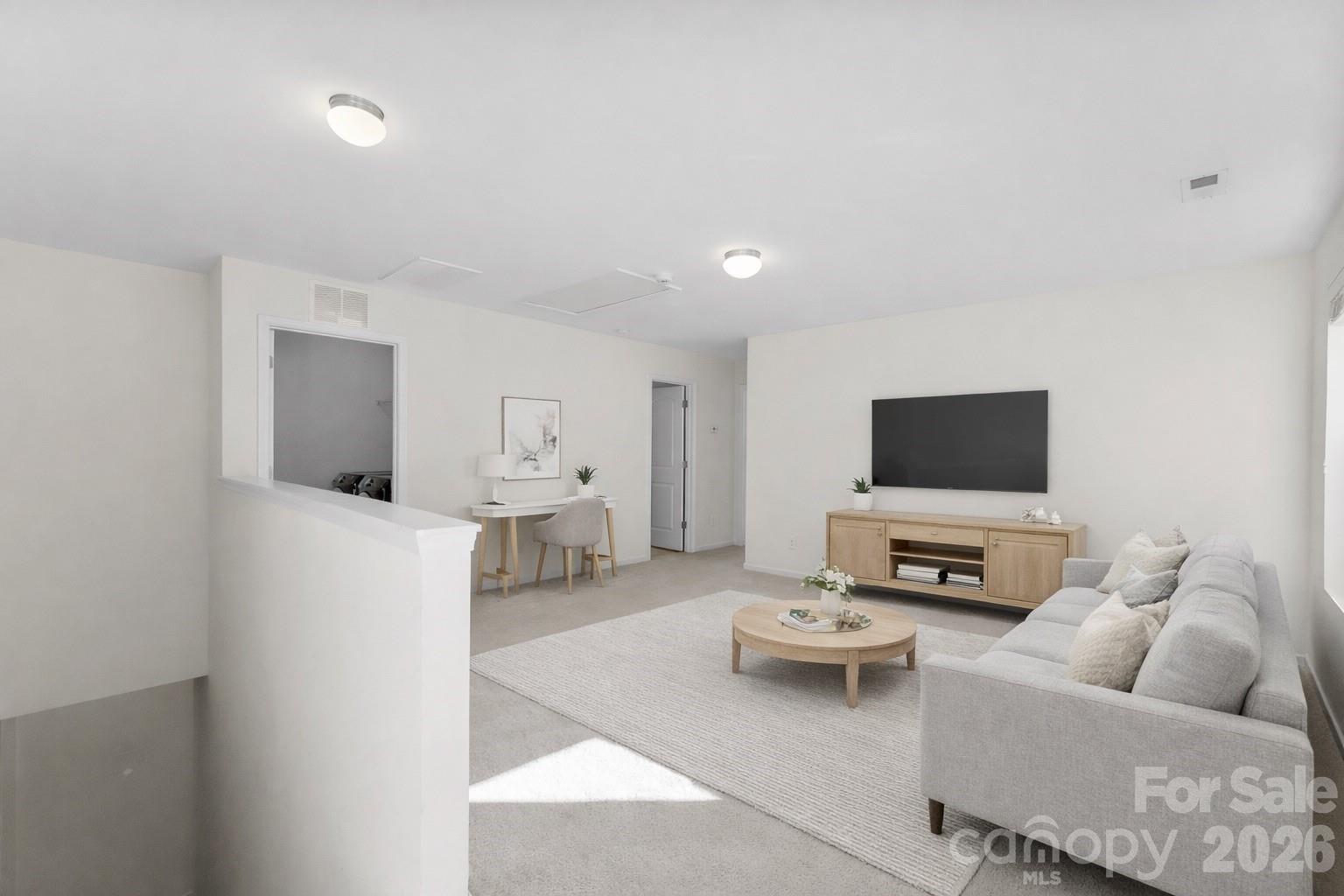 Staged living room with a gray sectional, wall-mounted TV, and small desk behind a half wall.