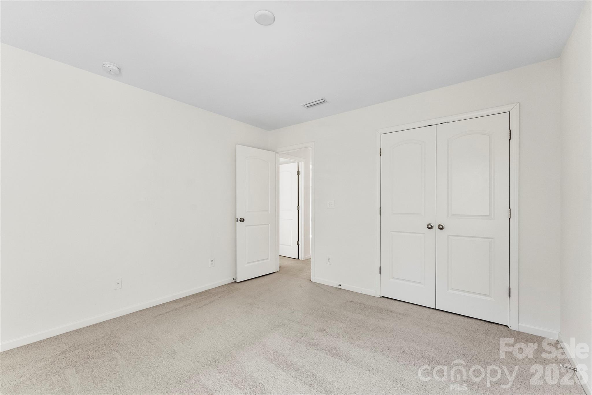 Empty carpeted bedroom with white walls, an open doorway, and double closet doors.