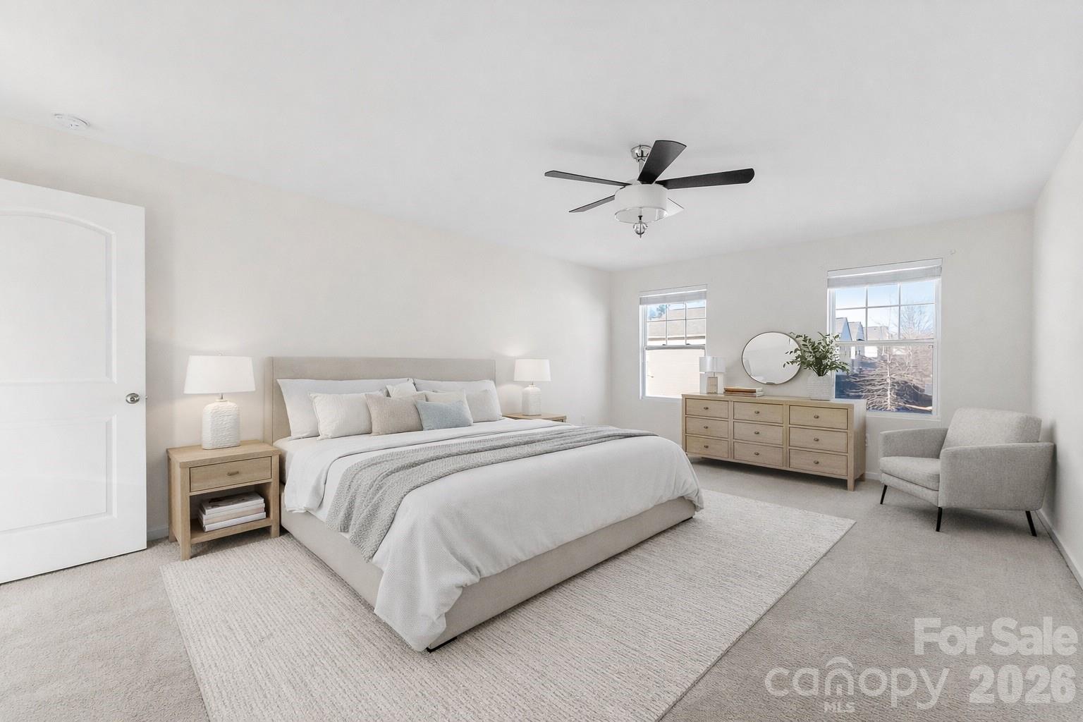 Furnished bedroom with a large bed, neutral decor, ceiling fan, and two windows.