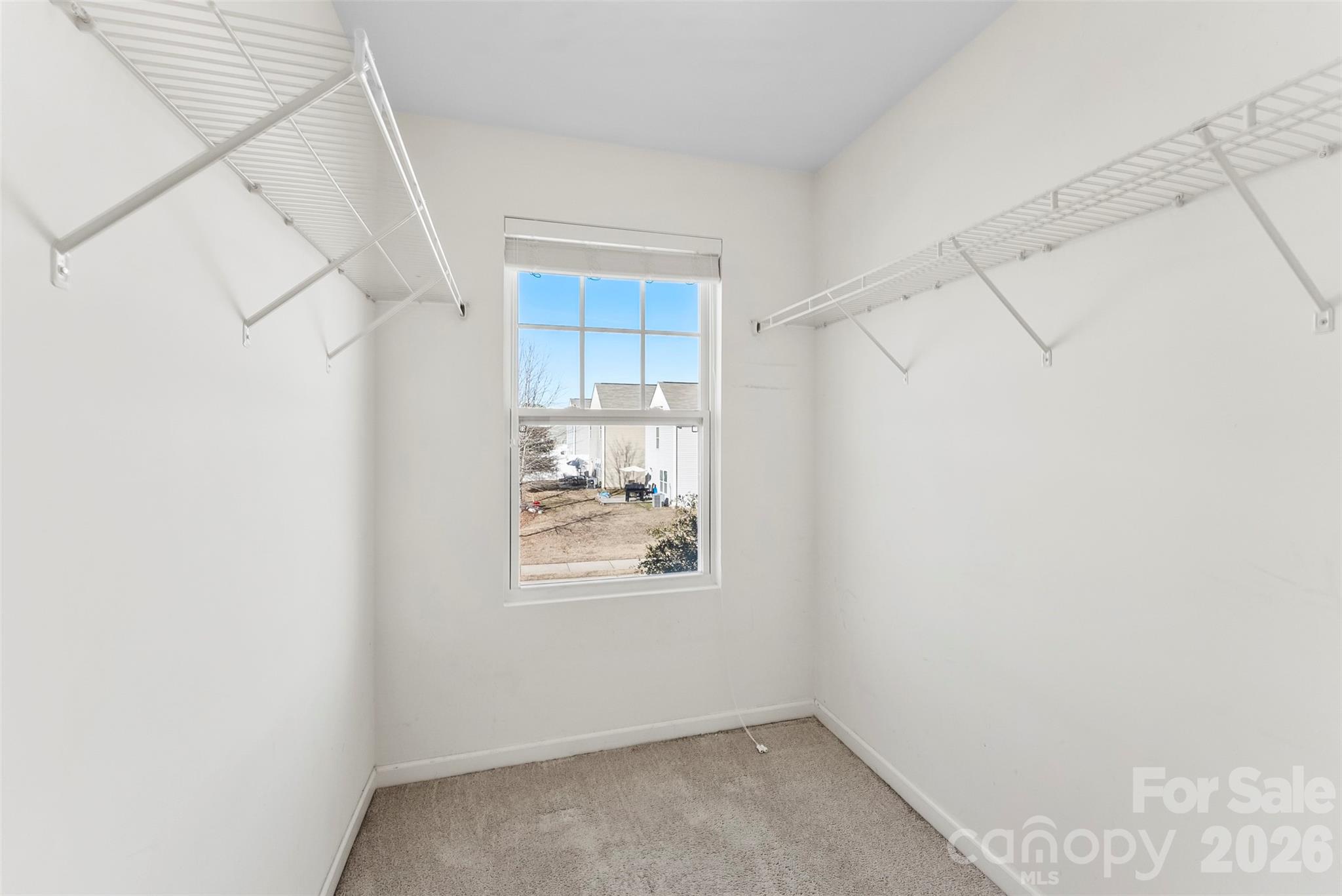 Empty walk-in closet with wire shelving on both sides and a window.