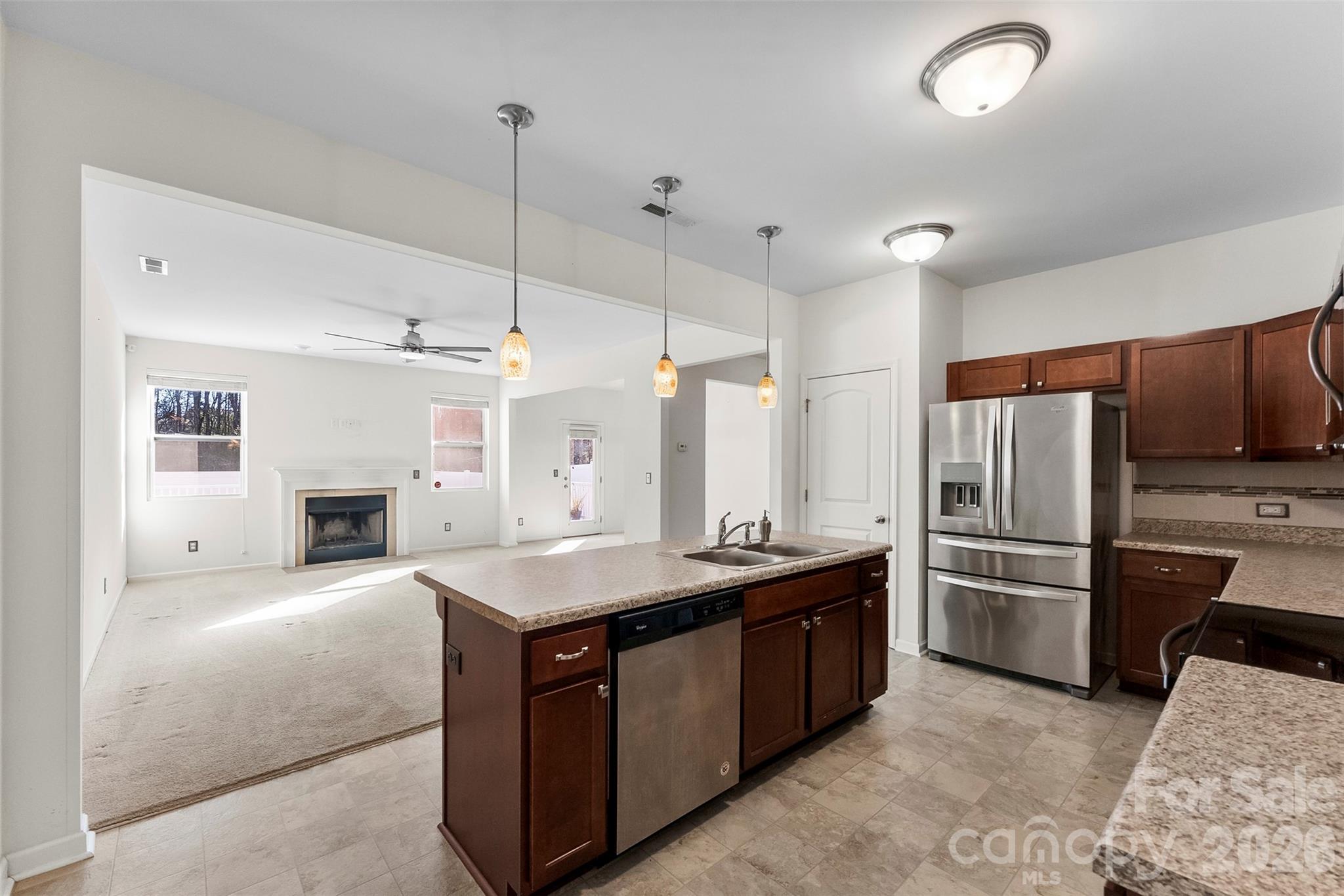 Open-plan kitchen and living room with a central island, stainless steel appliances, and a fireplace.