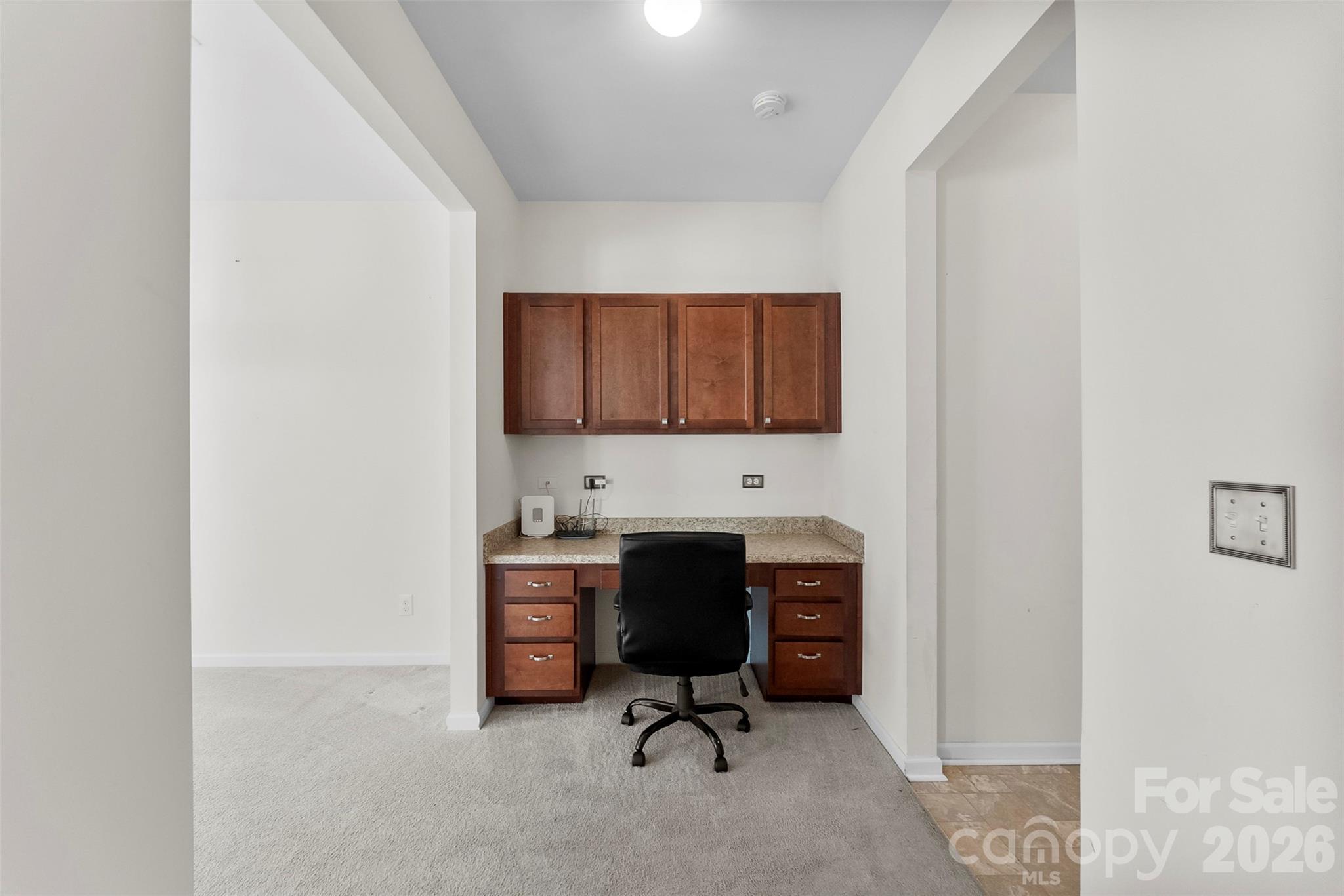 Home office with built-in wooden desk and cabinets, black rolling chair, and carpeted floor.