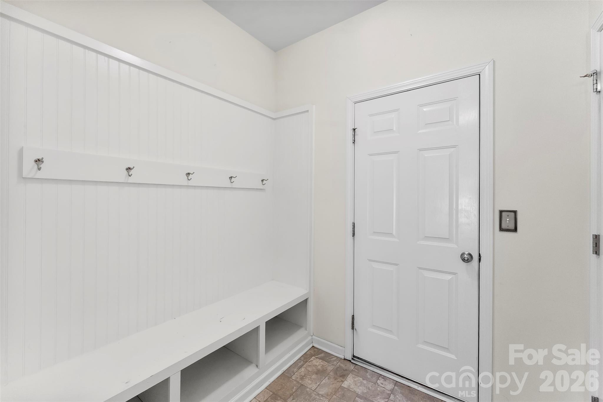Entryway with a built-in white bench, cubbies, coat hooks, and paneled door.