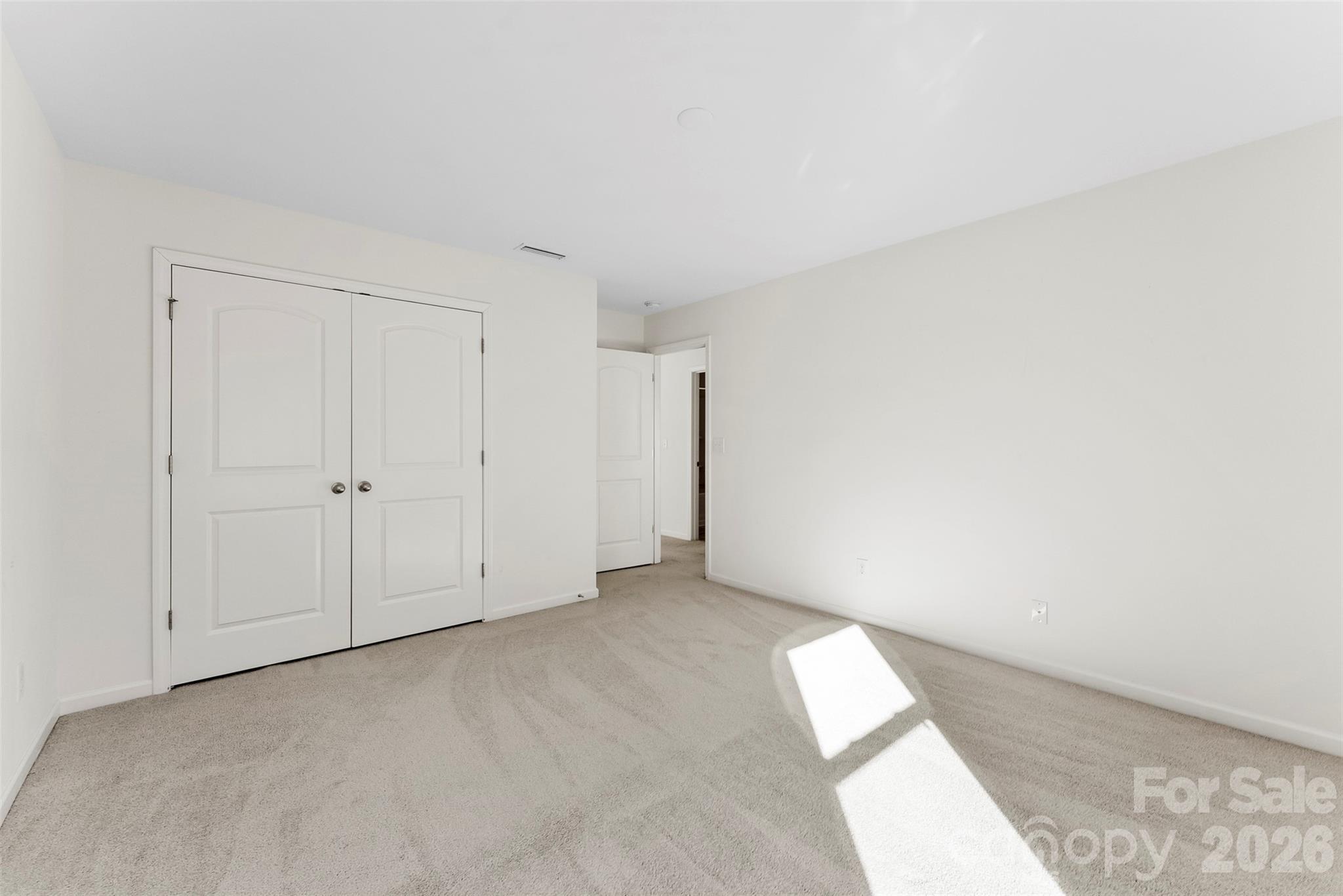 Empty carpeted bedroom with white double closet doors and sunlight across the floor.