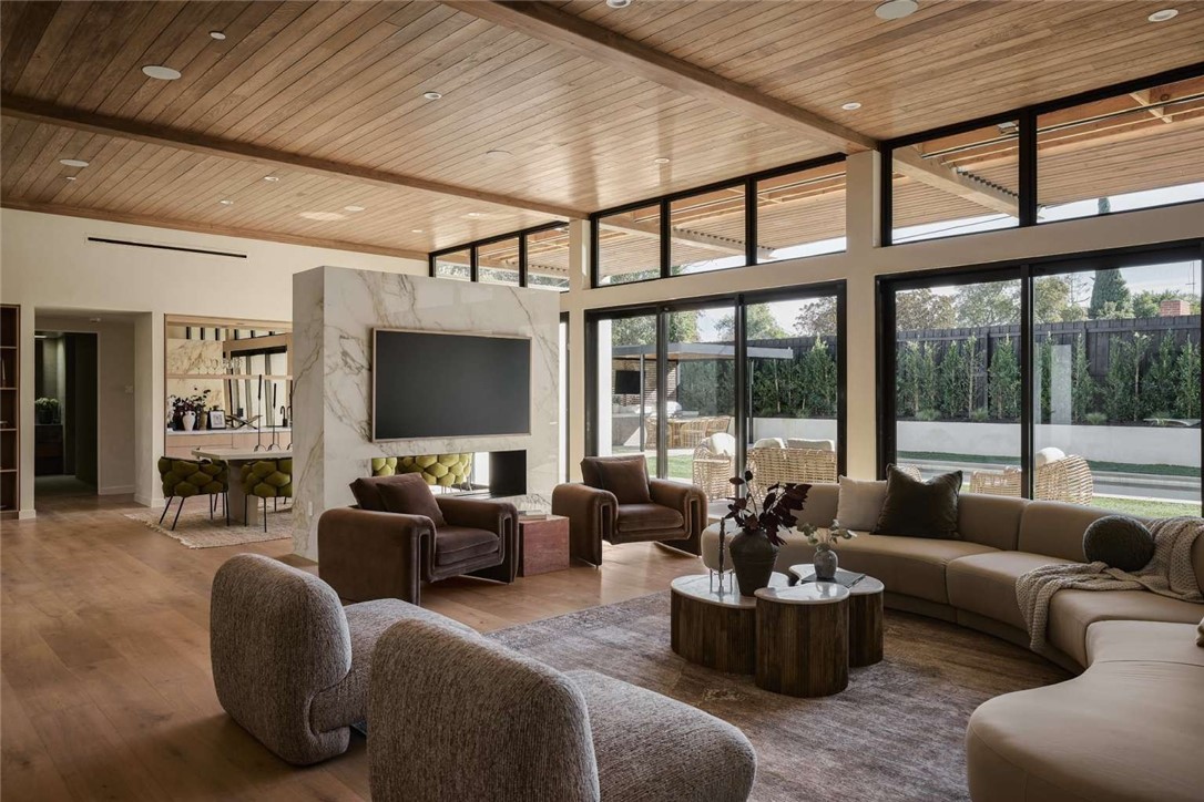 Living room with a wood-plank ceiling, marble fireplace wall, and large windows overlooking the backyard.