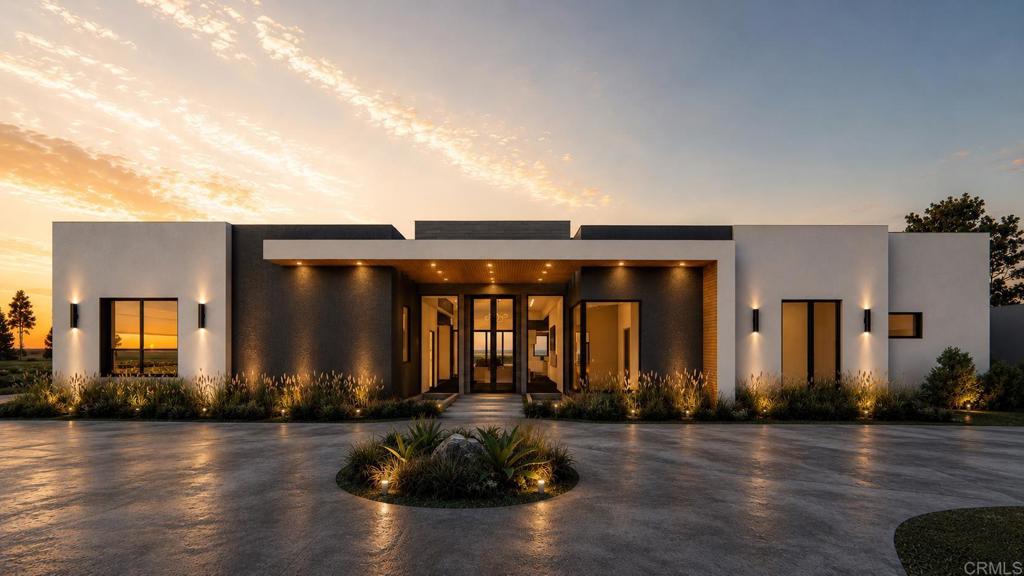 Modern home with a recessed, warmly lit entry and landscaped driveway at dusk.