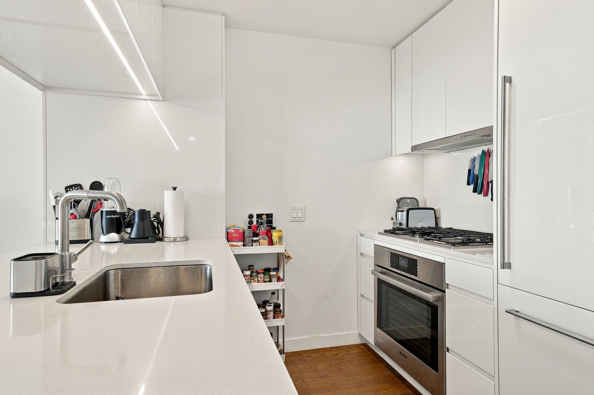 Modern white kitchen with a long counter, stainless steel sink, and built-in gas cooktop and oven.