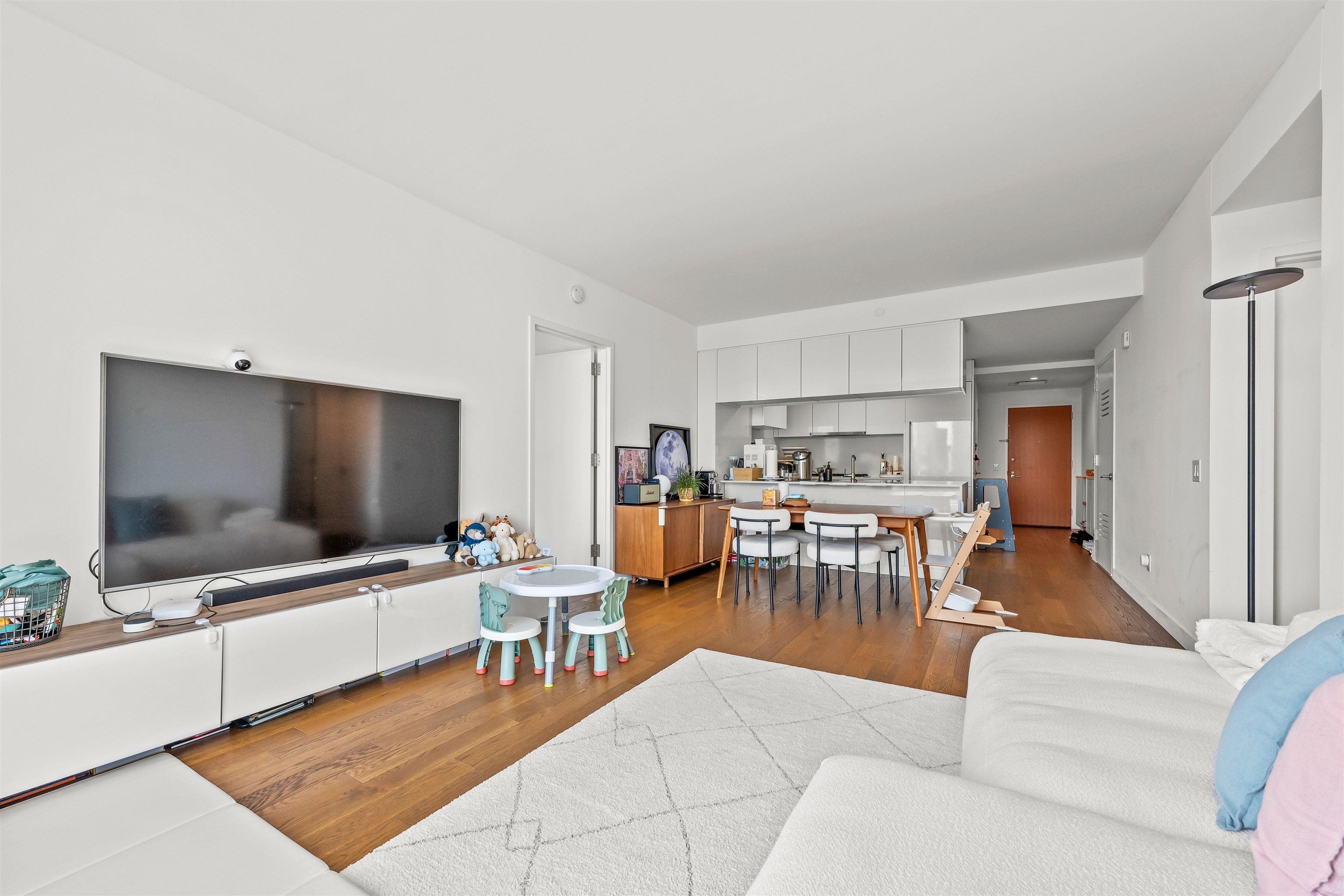 Open-plan living room and kitchen with hardwood floors, white sectional, and dining area.
