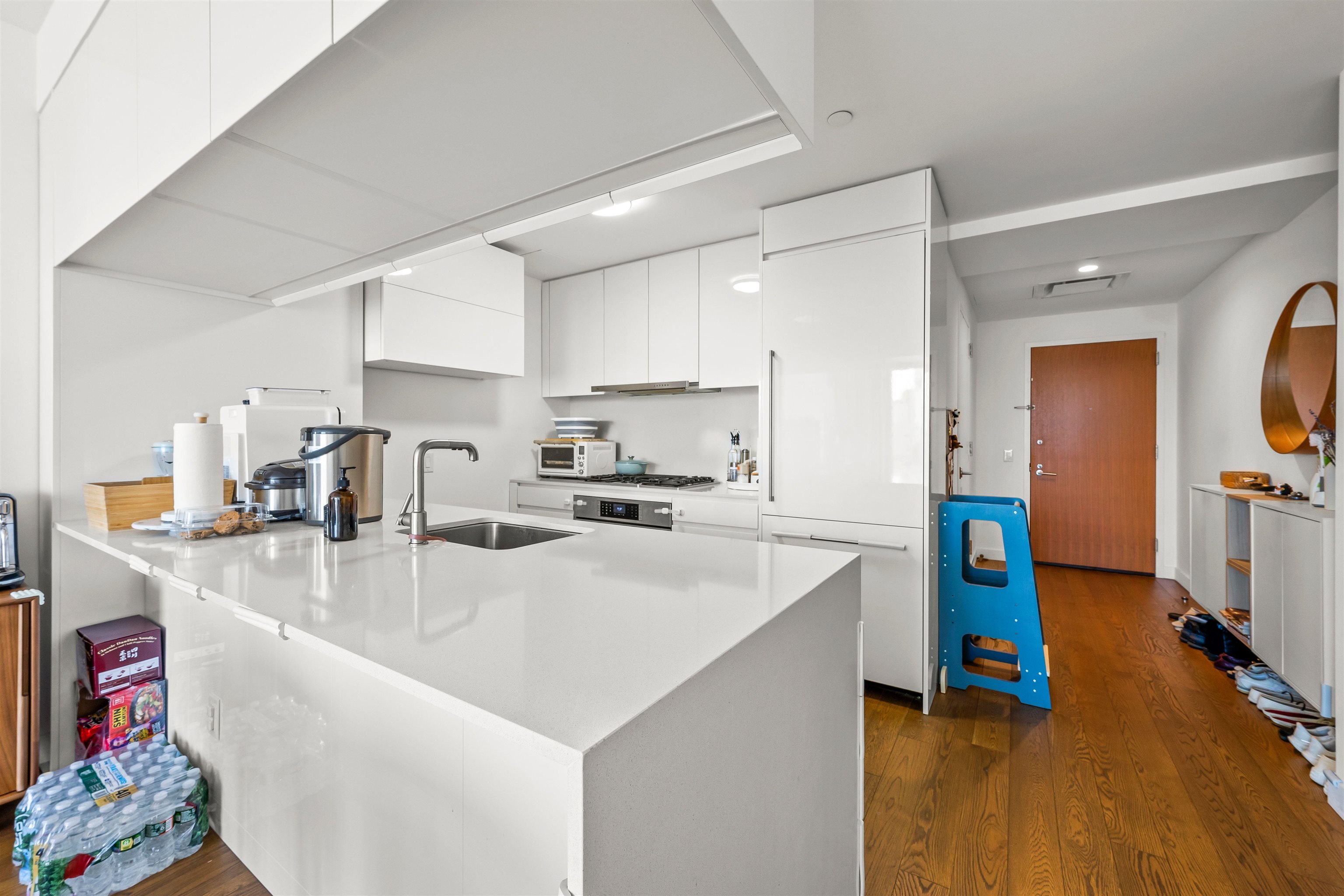 Modern white kitchen with a large island, built-in appliances, and warm wood flooring.