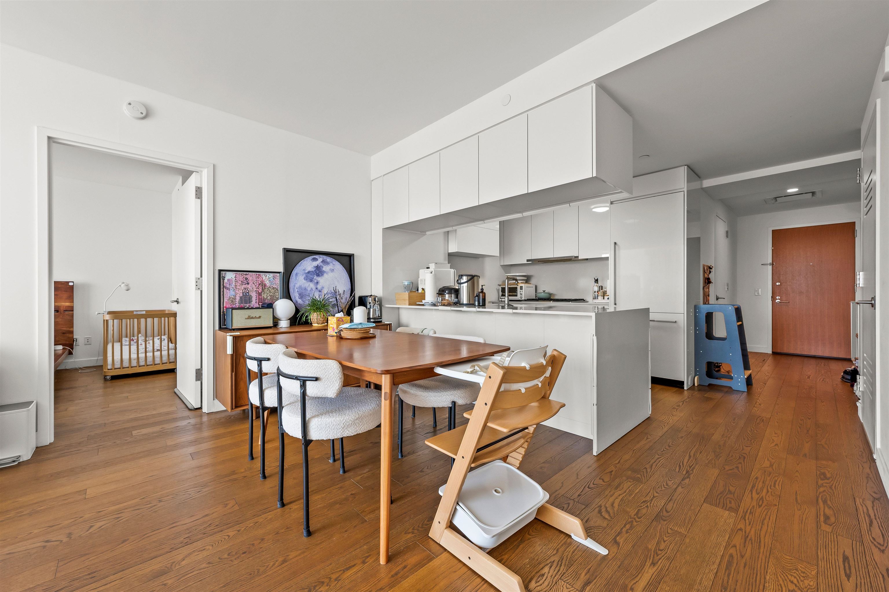 Open-plan kitchen and dining area with white cabinetry, a wood table, and a nursery doorway.