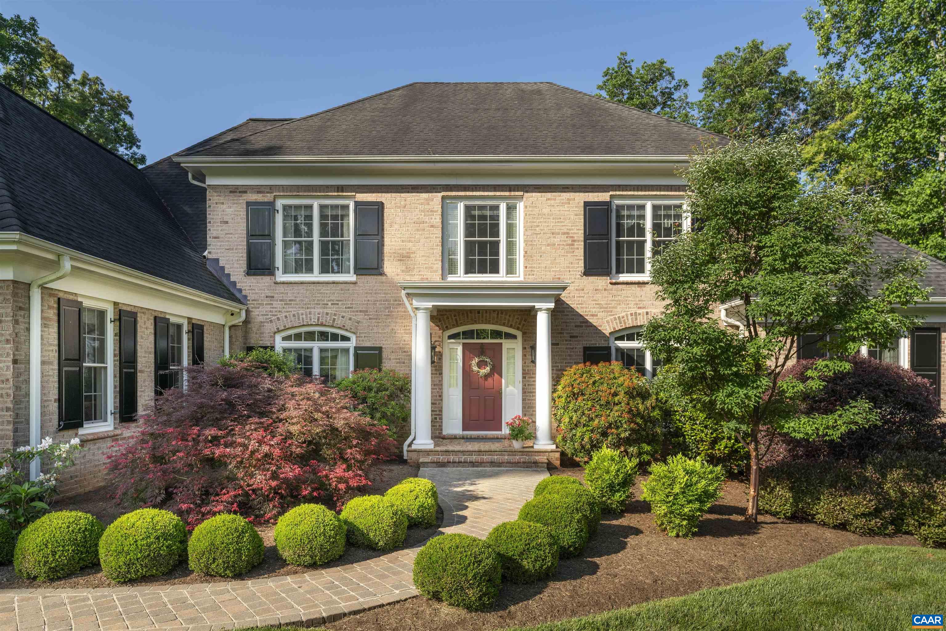 Two-story brick home with a red front door, white-columned entry, and landscaped brick walkway.