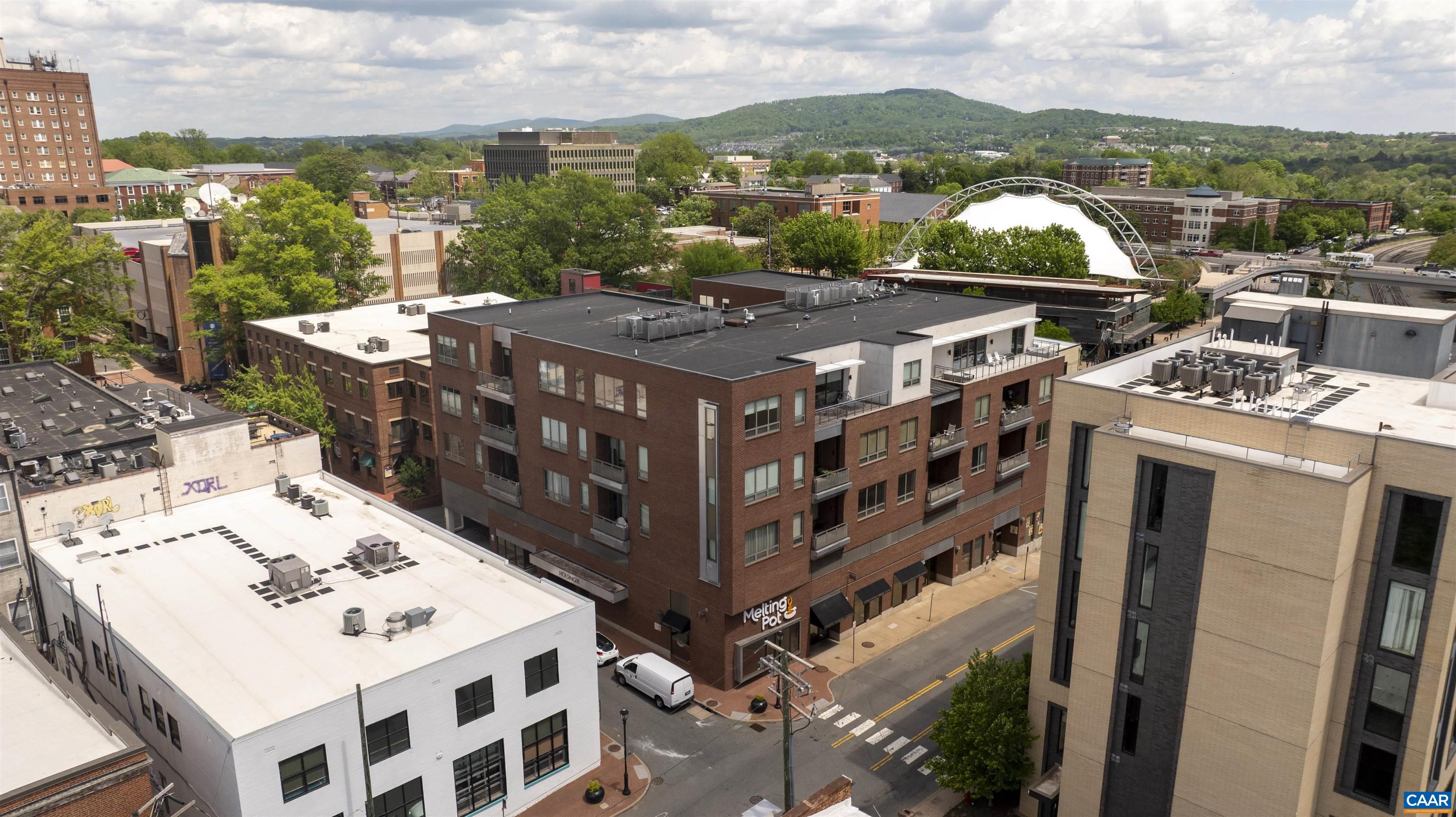 Aerial downtown view of brick buildings and a white arched canopy, with wooded hills beyond.