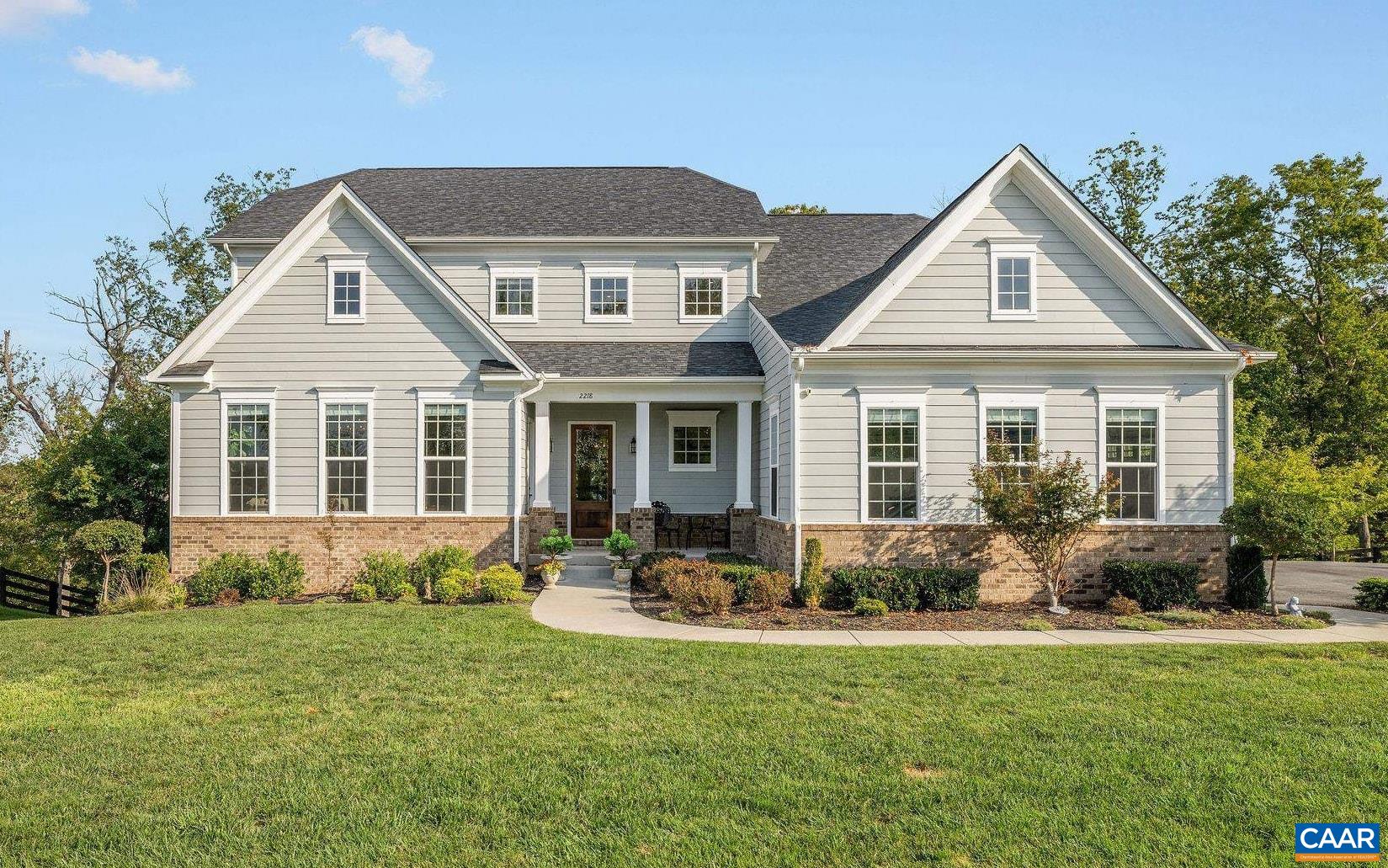 Light-colored gabled house with a brick foundation, landscaped entry, and broad green lawn.