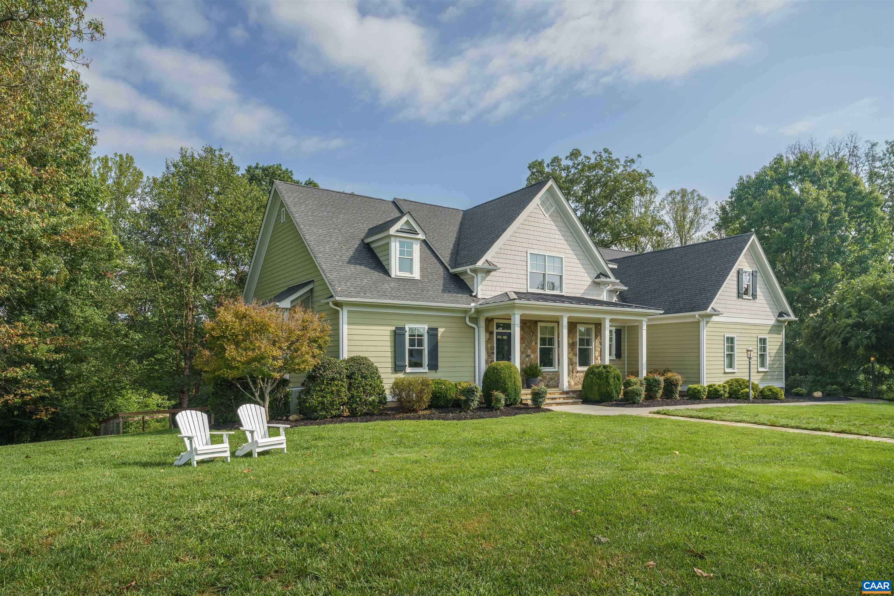 Light-green gabled house with a stone-accented porch, landscaped lawn, and two white Adirondack chairs.