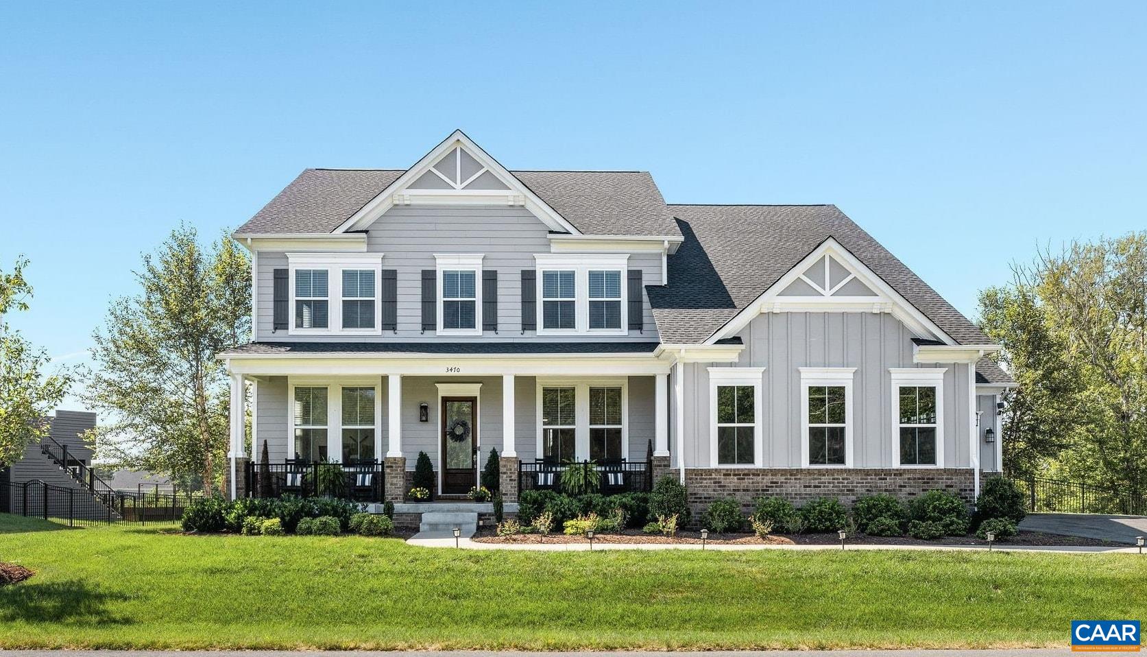 Gray and white two-story house with a covered porch, dark shutters, and landscaped front lawn.