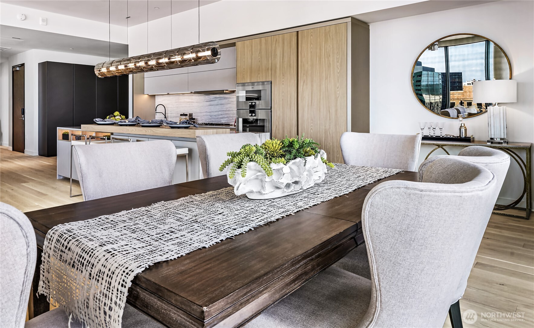 Dining room with a dark wood table and white chairs beside a modern kitchen with light wood cabinets.