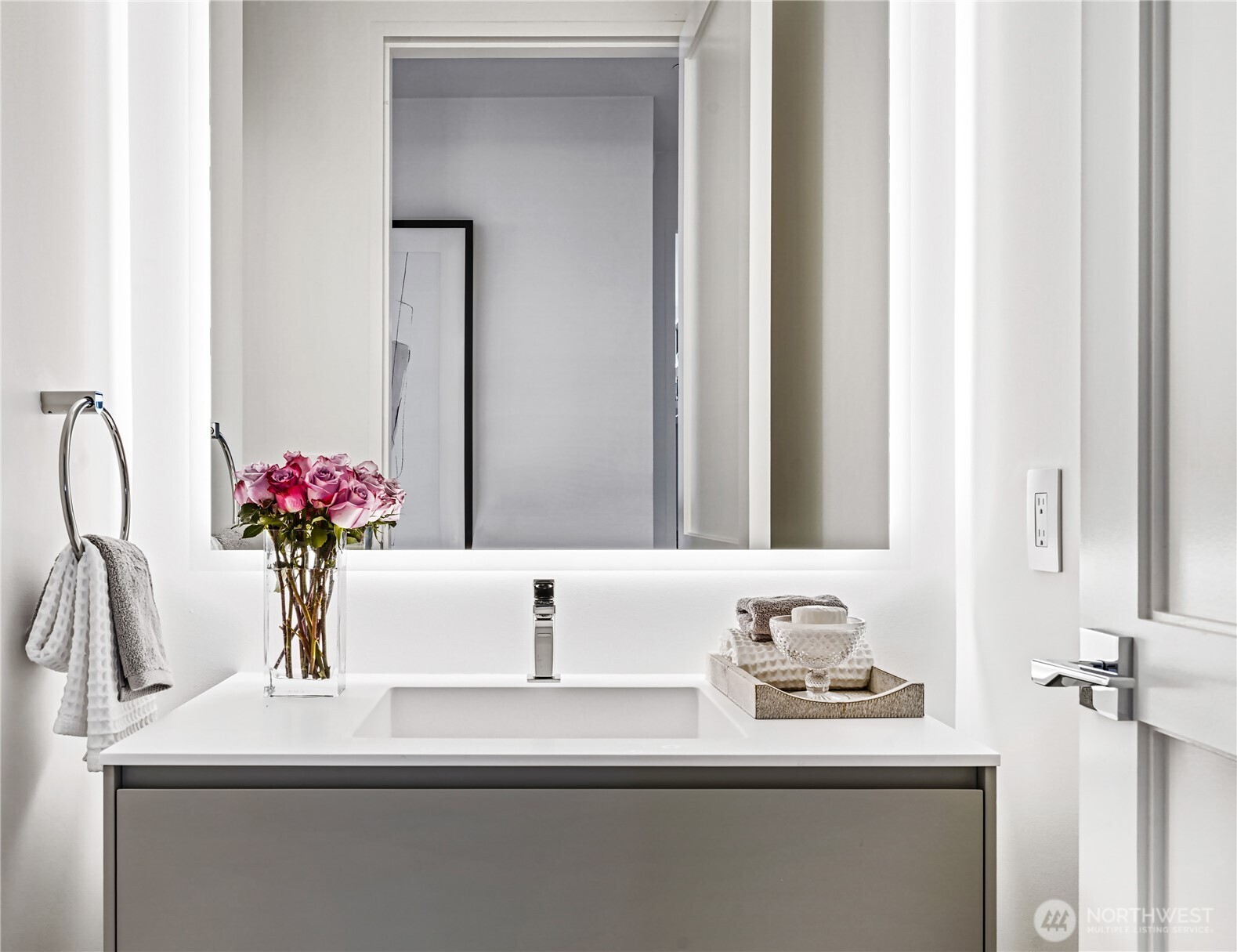 Modern bathroom vanity with a large mirror, chrome fixtures, and pink roses beside the sink.